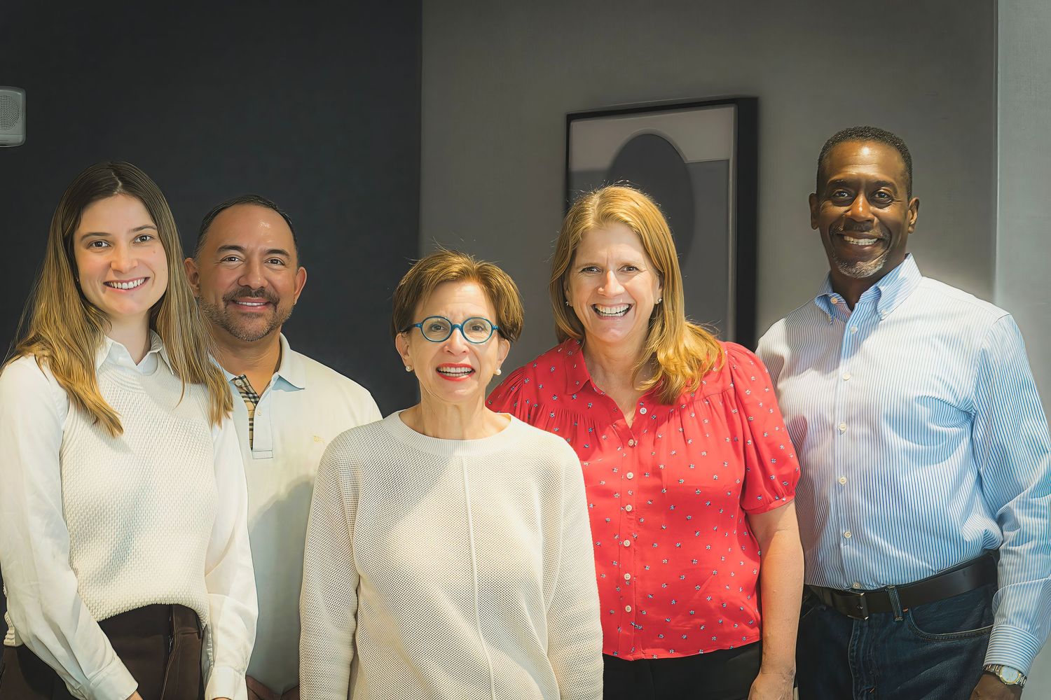 Five diverse business professionals smiling together for a group photo in a modern office.