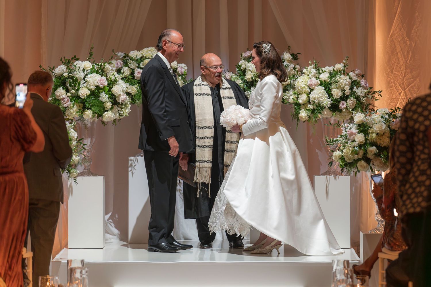 Couple exchanges vows at elegant Jewish wedding ceremony with white floral arrangements.
