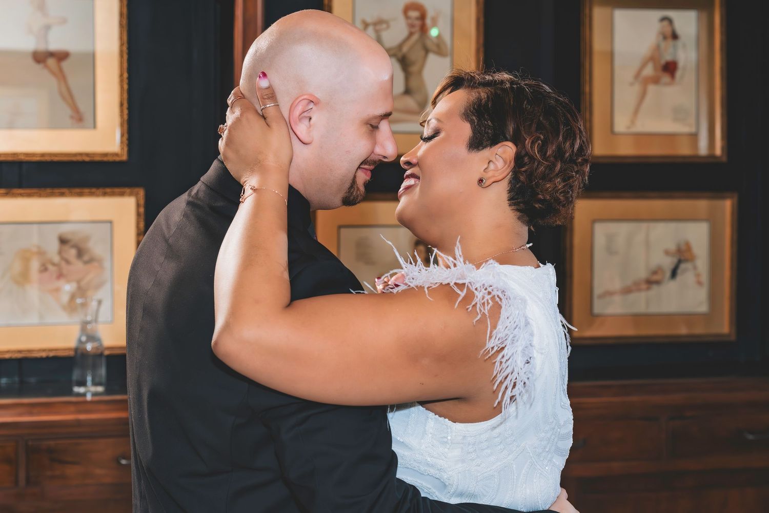 Bride and groom share a joyful embrace surrounded by framed artwork at their wedding reception.