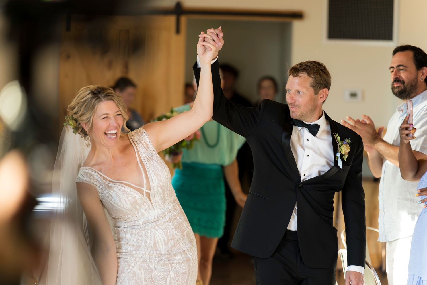 Bride and groom raising hands in celebration during wedding reception first dance with guests cheering.