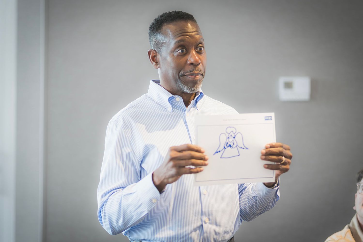 Man in blue shirt presenting a hand-drawn sketch during a business meeting or workshop presentation.