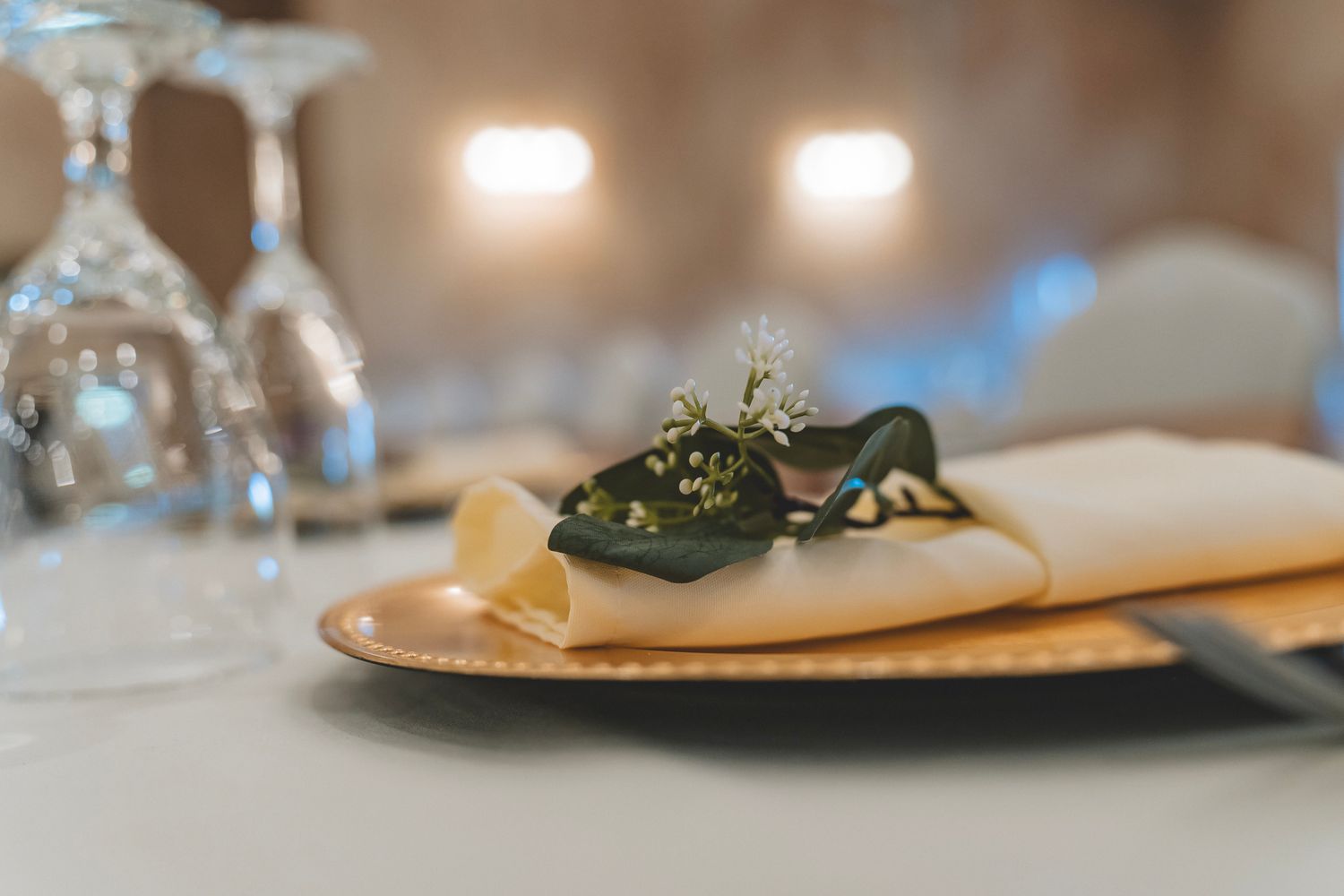 Elegant table setting with folded napkin, floral accent, gold plate, and wine glasses.