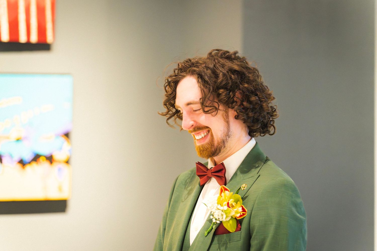 Happy groom in green suit and burgundy bow tie laughs joyfully on wedding day.