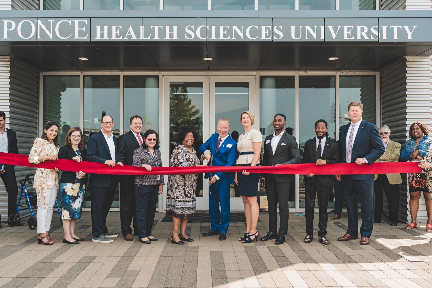 Group of professionals celebrate ribbon cutting ceremony outside Ponce Health Sciences University entrance.