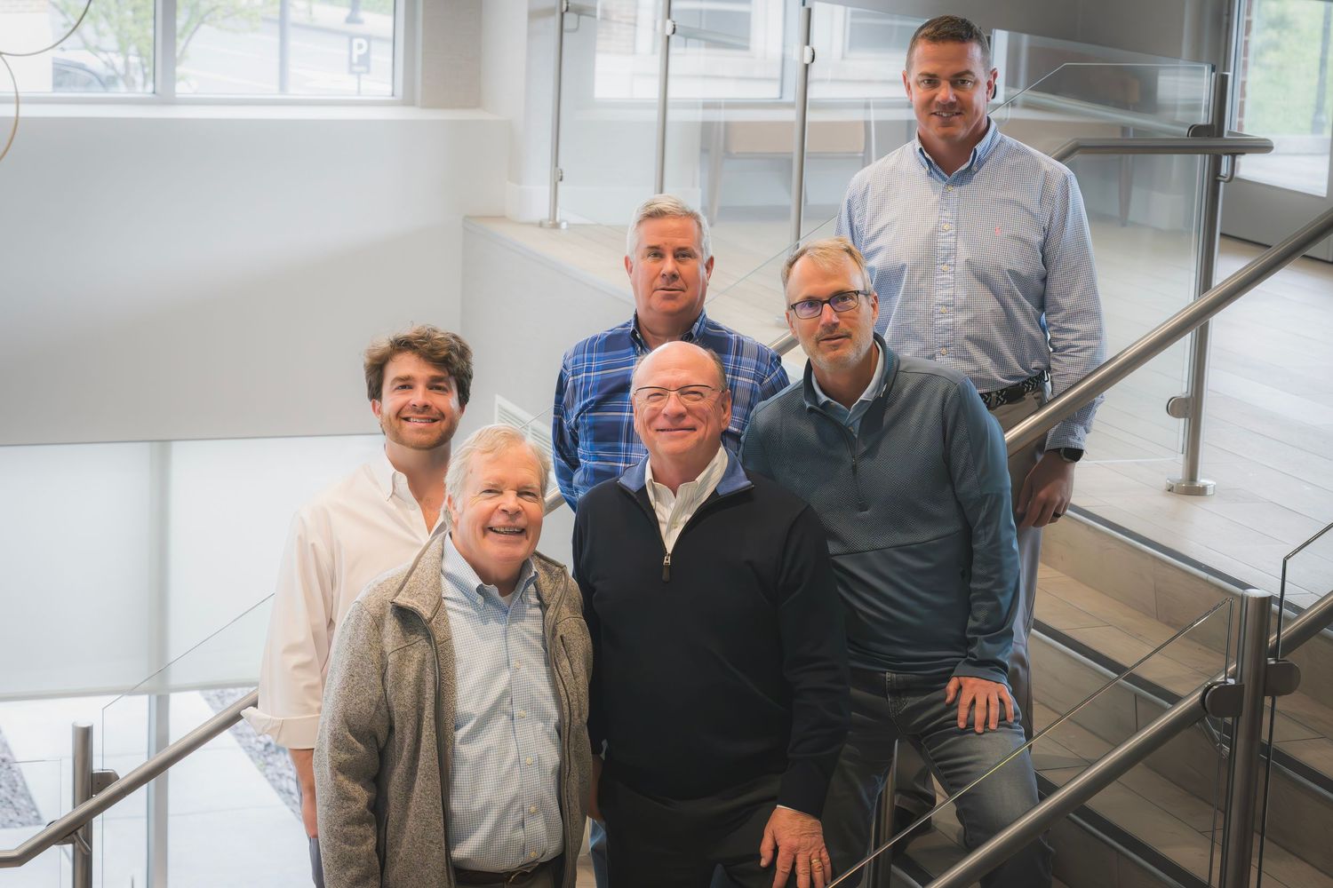 Group of six men posing together on a modern office staircase for a professional team photo.