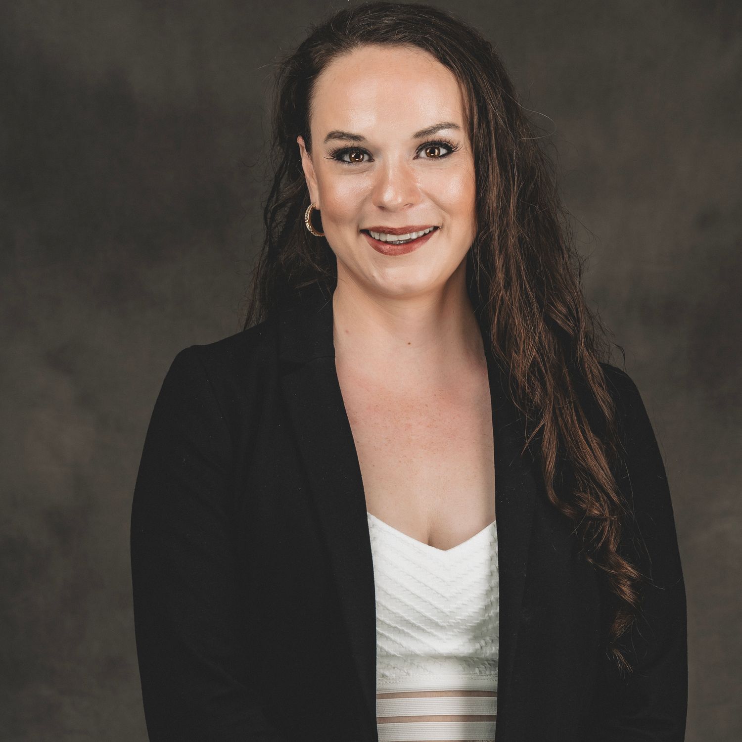 Professional headshot of a smiling woman with long brown hair wearing a black blazer and white top.