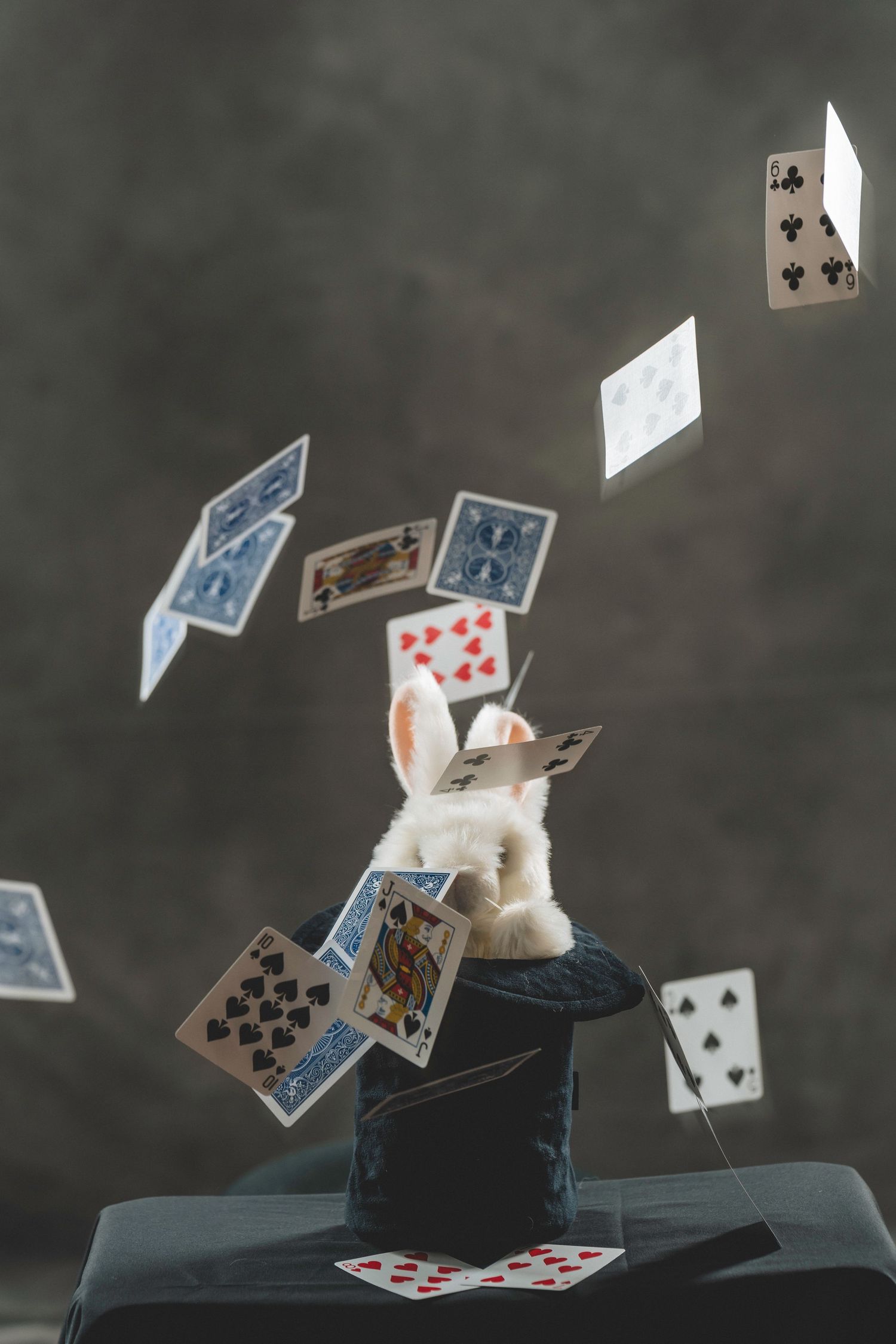 White rabbit emerging from magician hat with playing cards flying through the air.