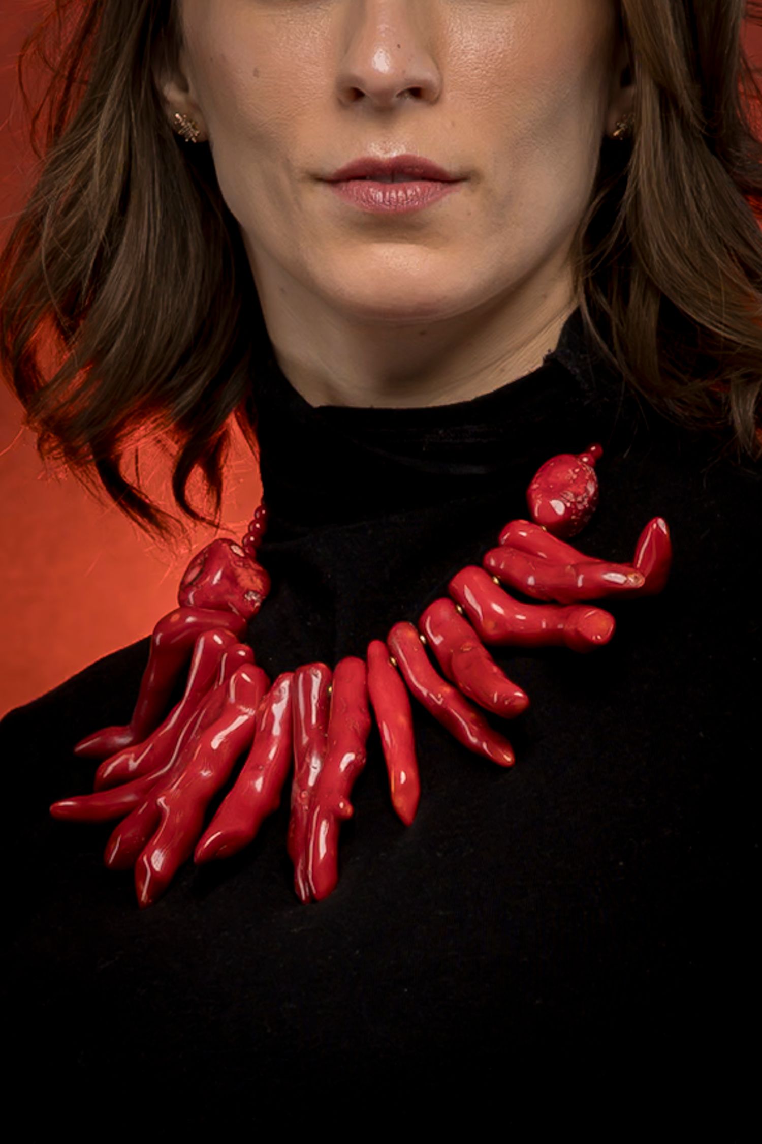 Woman wearing striking red coral branch statement necklace over black turtleneck.