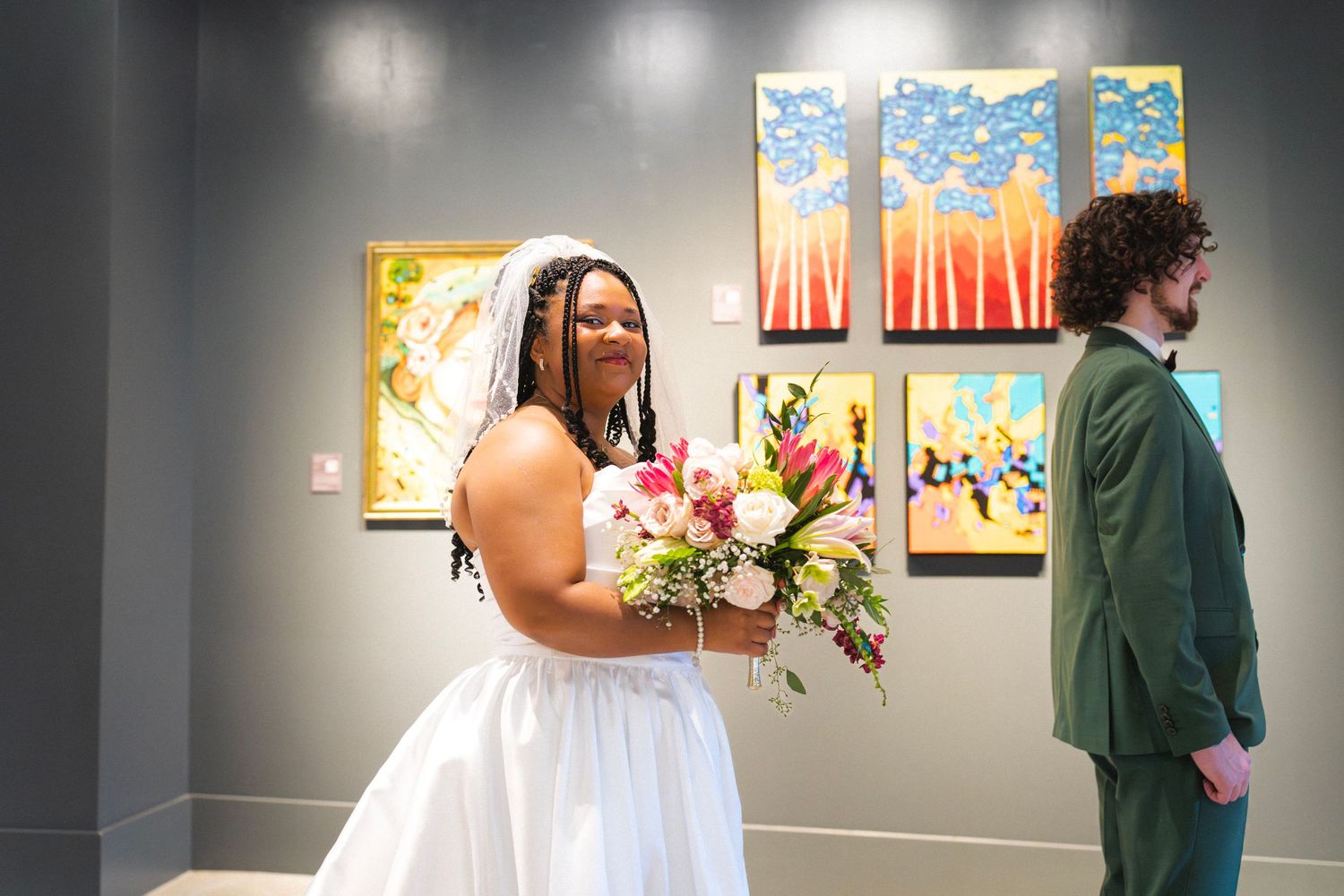 Bride holds colorful bouquet while standing near groom in gallery with vibrant artwork.