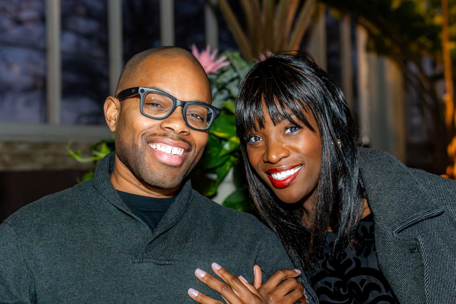 Smiling couple in matching dark outfits posing together at evening event outdoors.