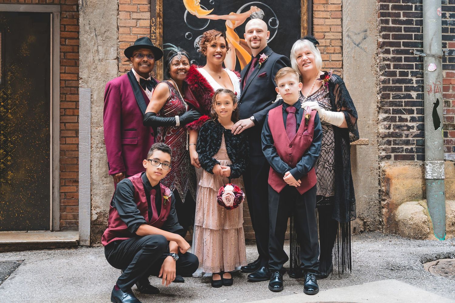 Wedding party group photo featuring family members in burgundy and black formal attire outdoors.