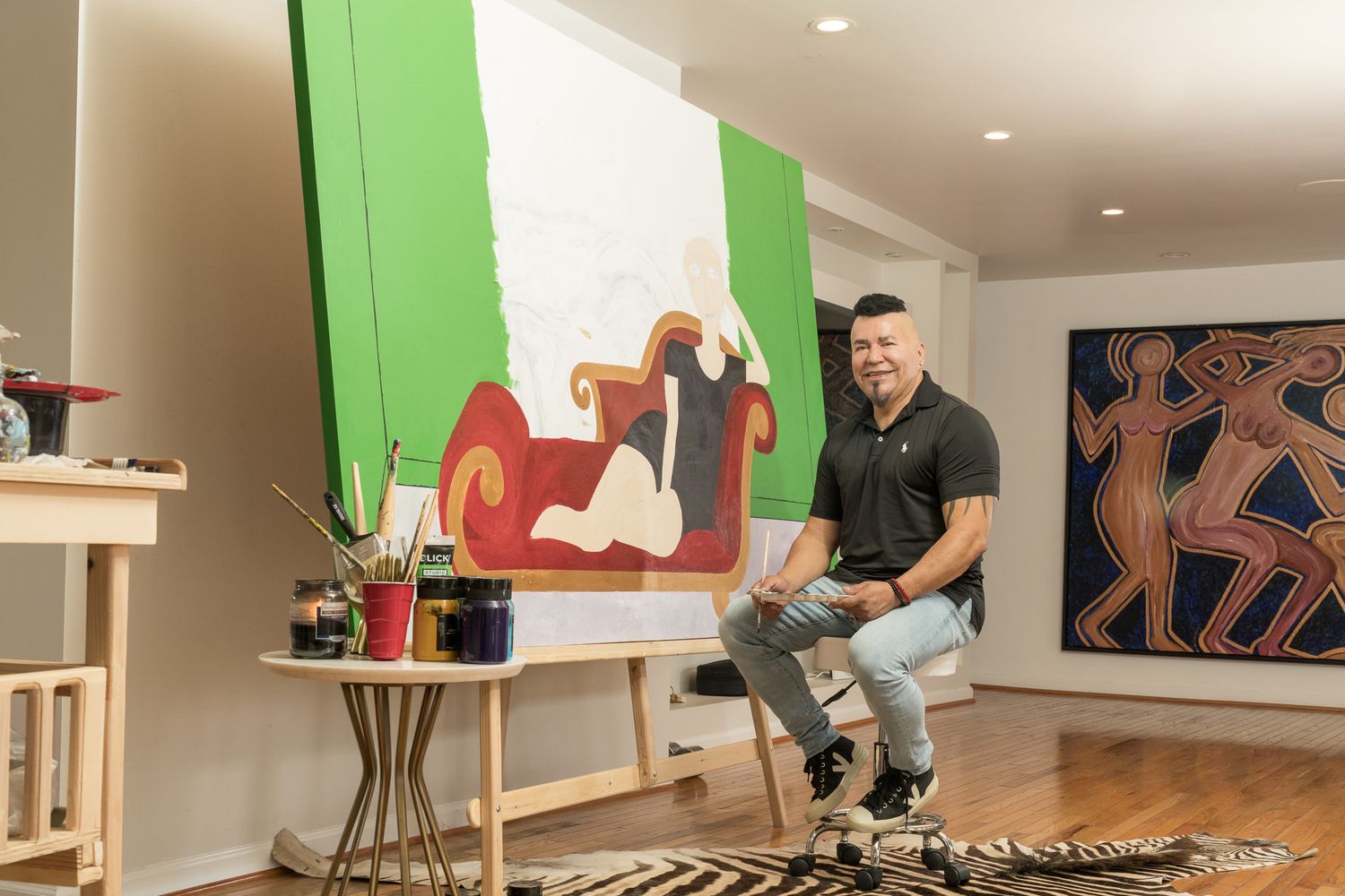 Male artist crouching beside large green and white canvas painting in studio.