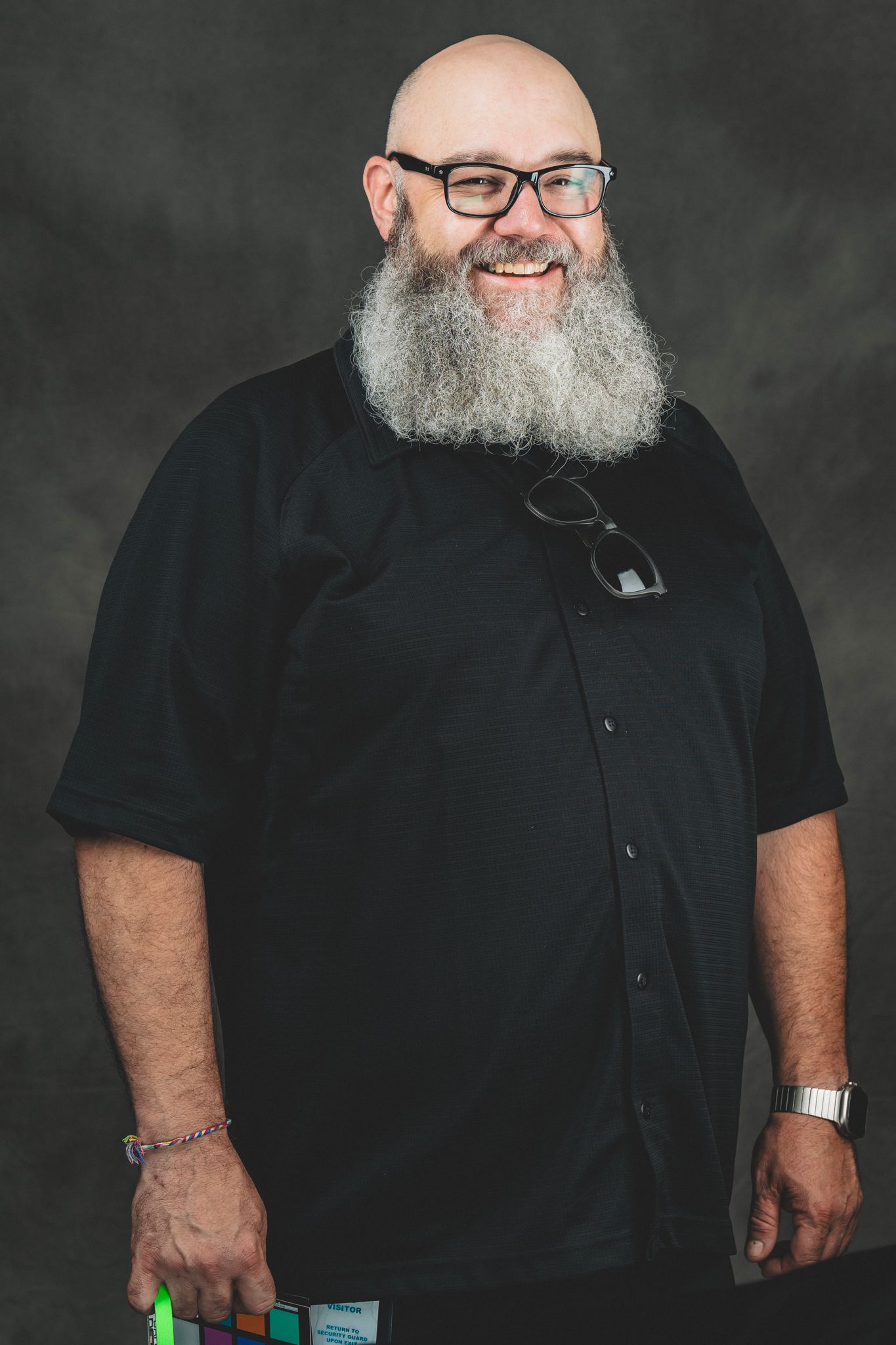 Bald man with a large gray beard smiling in a black shirt, wearing glasses and holding color swatches.