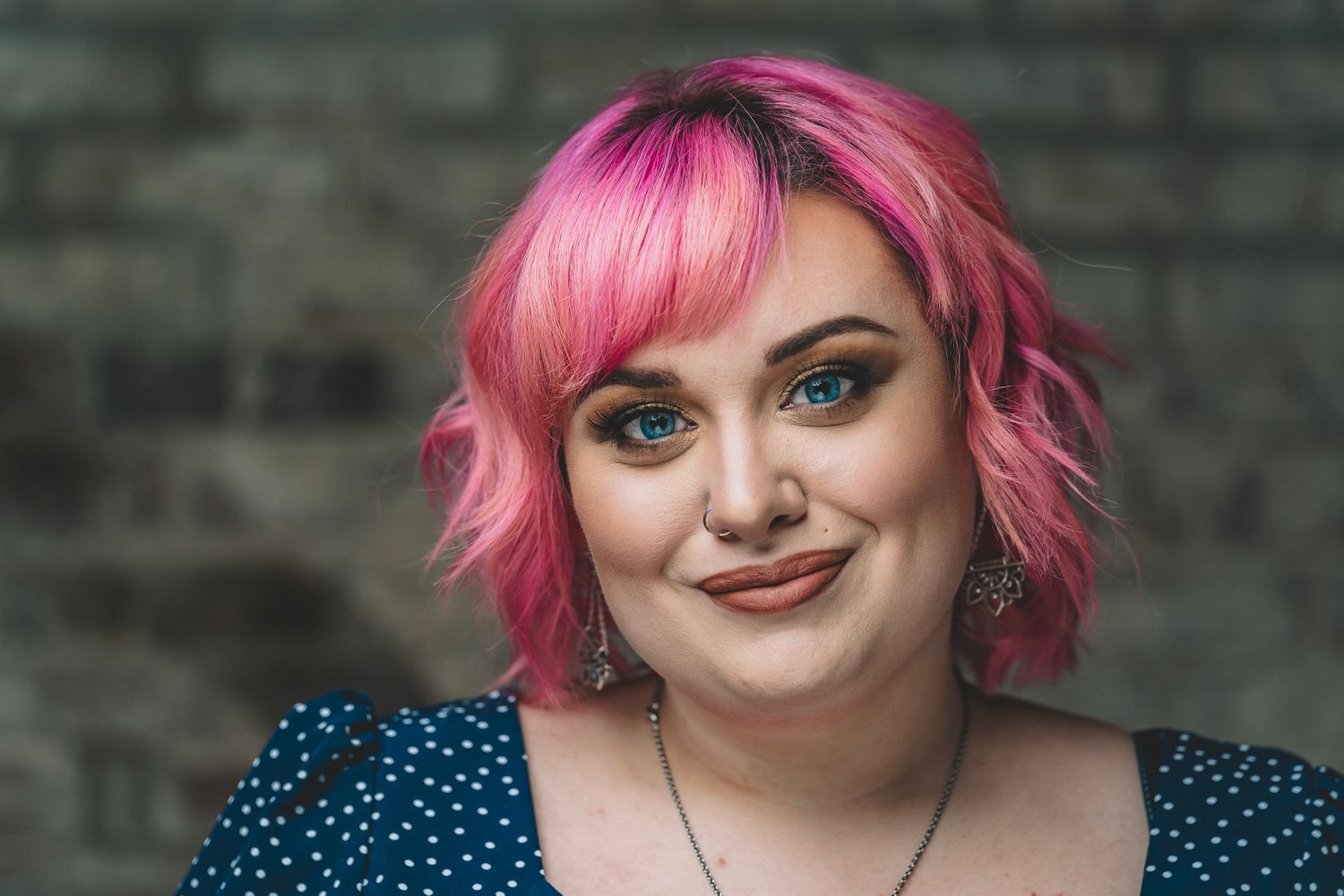 Young woman with pink hair and blue eyes smiling in a casual outdoor portrait.