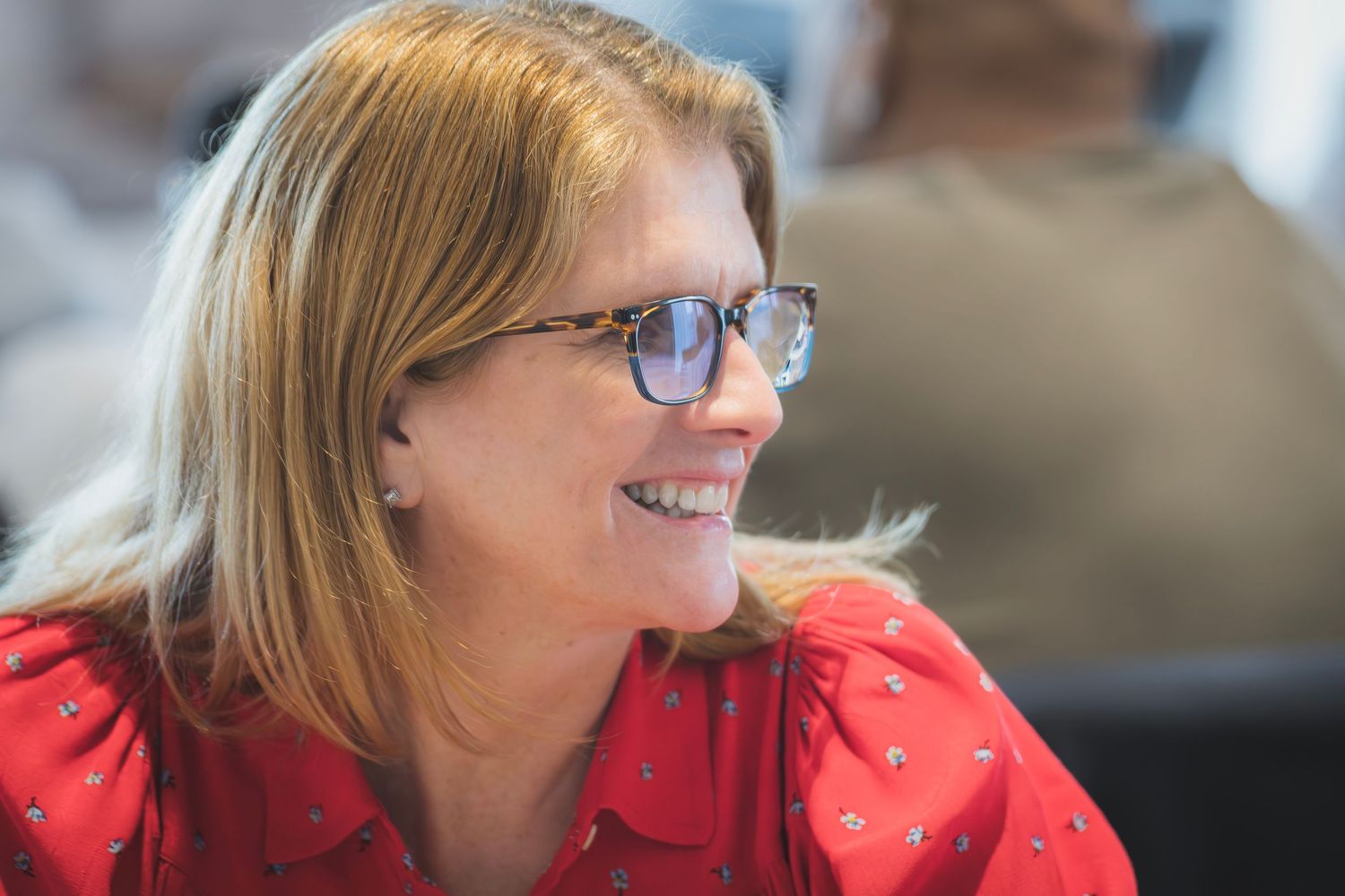 Smiling woman with glasses wearing red blouse at professional business meeting or conference.