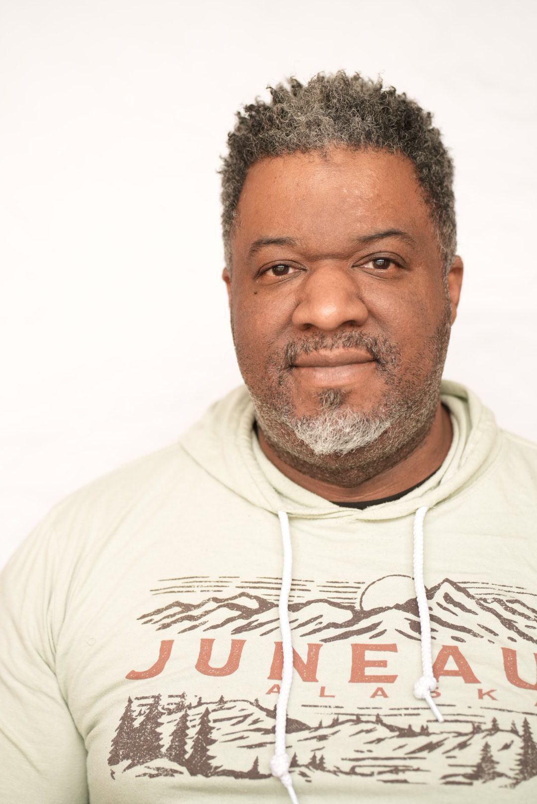 Middle-aged man wearing Juneau Alaska hoodie poses for portrait against white background.