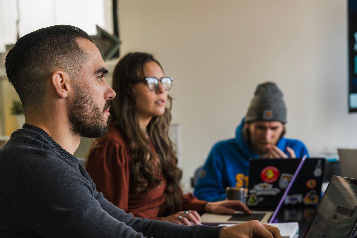 Three focused professionals working on laptops during a team meeting in a bright workspace.