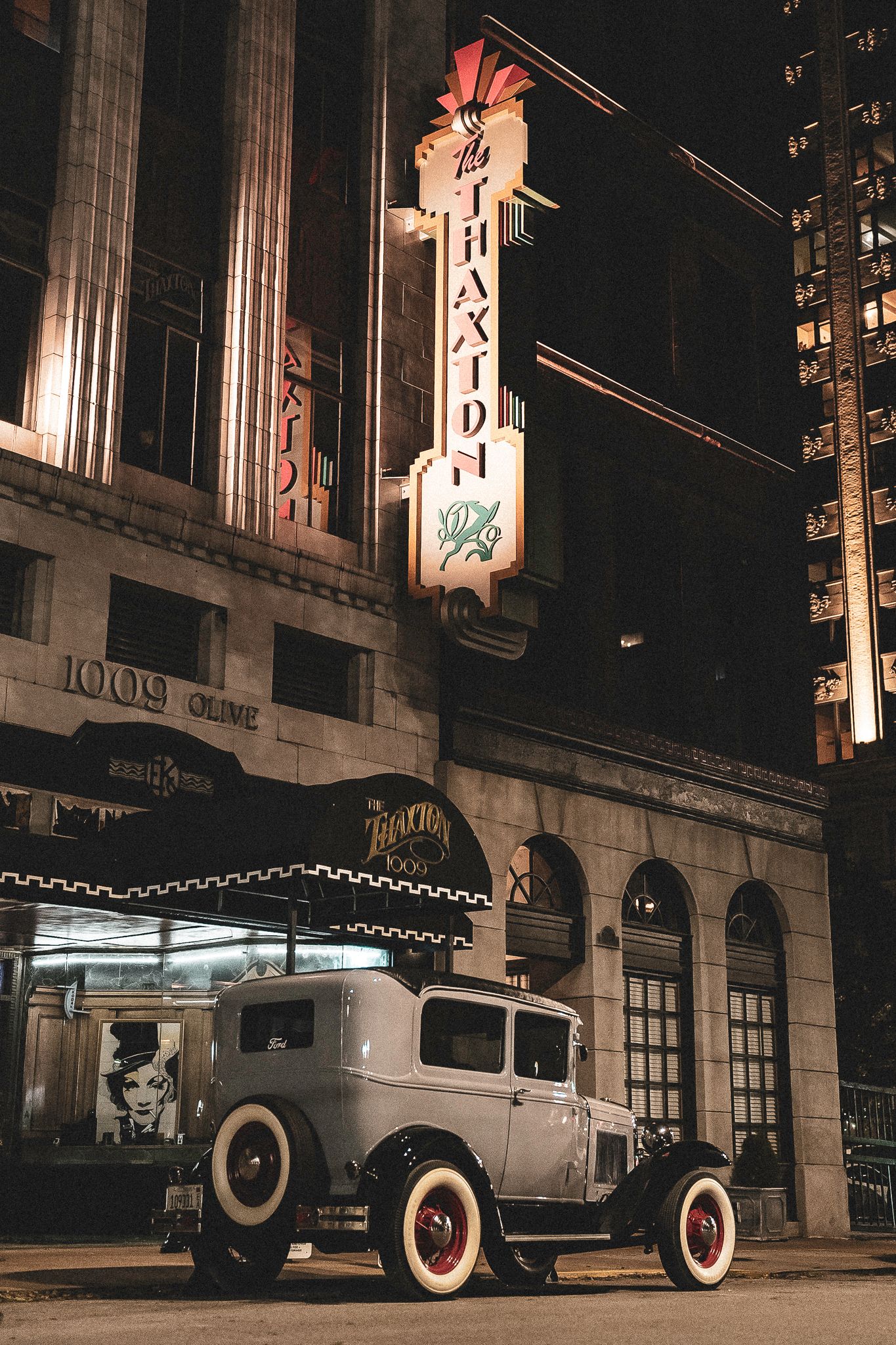 Vintage 1930s hot rod parked outside the Thaxton building at night, illuminated by neon signs in an urban setting.