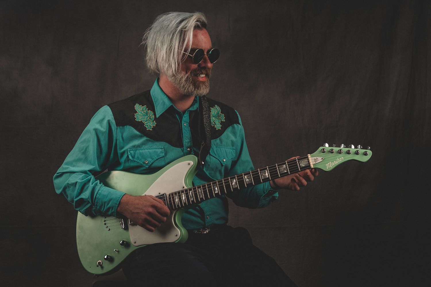 Senior musician with white hair playing white electric guitar in teal western shirt.