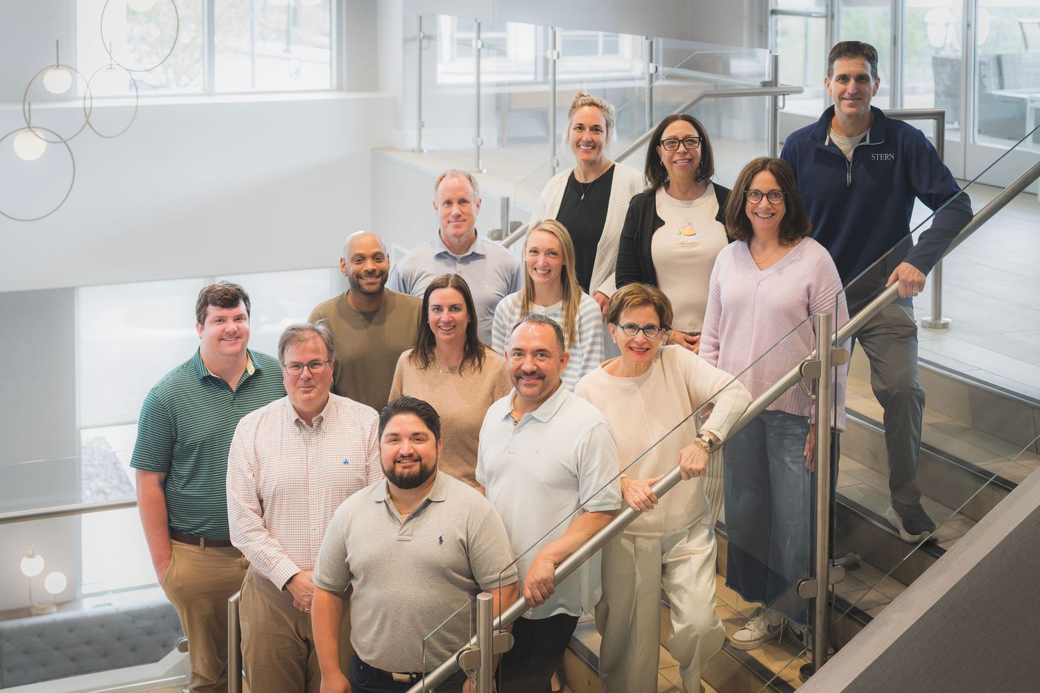 Large group of twelve business professionals posing on modern office staircase for team photo.