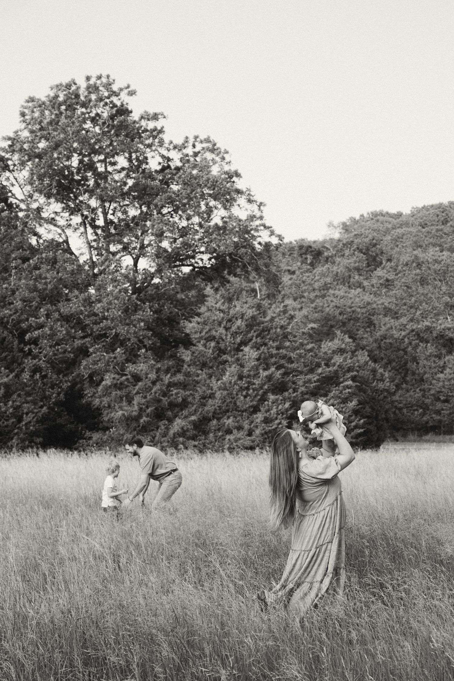 A family dances and plays together in a tall grass meadow with trees in the background.
