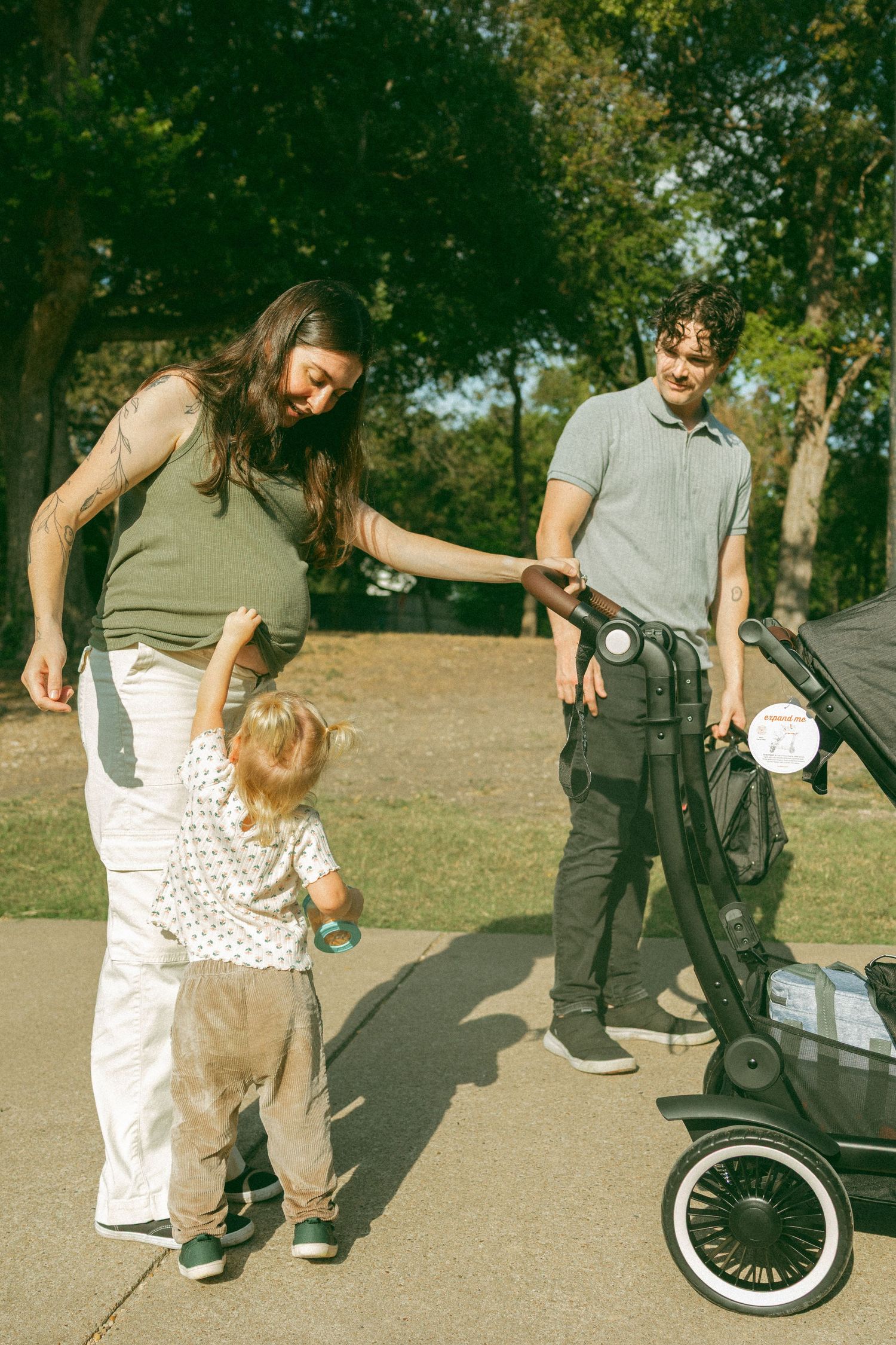 Toddler reaches up to give pregnant mom's belly love while family is on a walk at their favorite park in Pflugerville Texas.