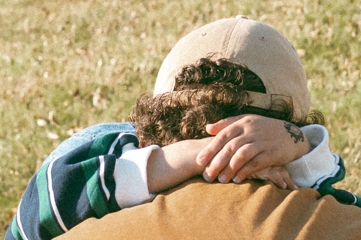 A person wearing a beige baseball cap lies on grass while looking upward on a sunny day.
