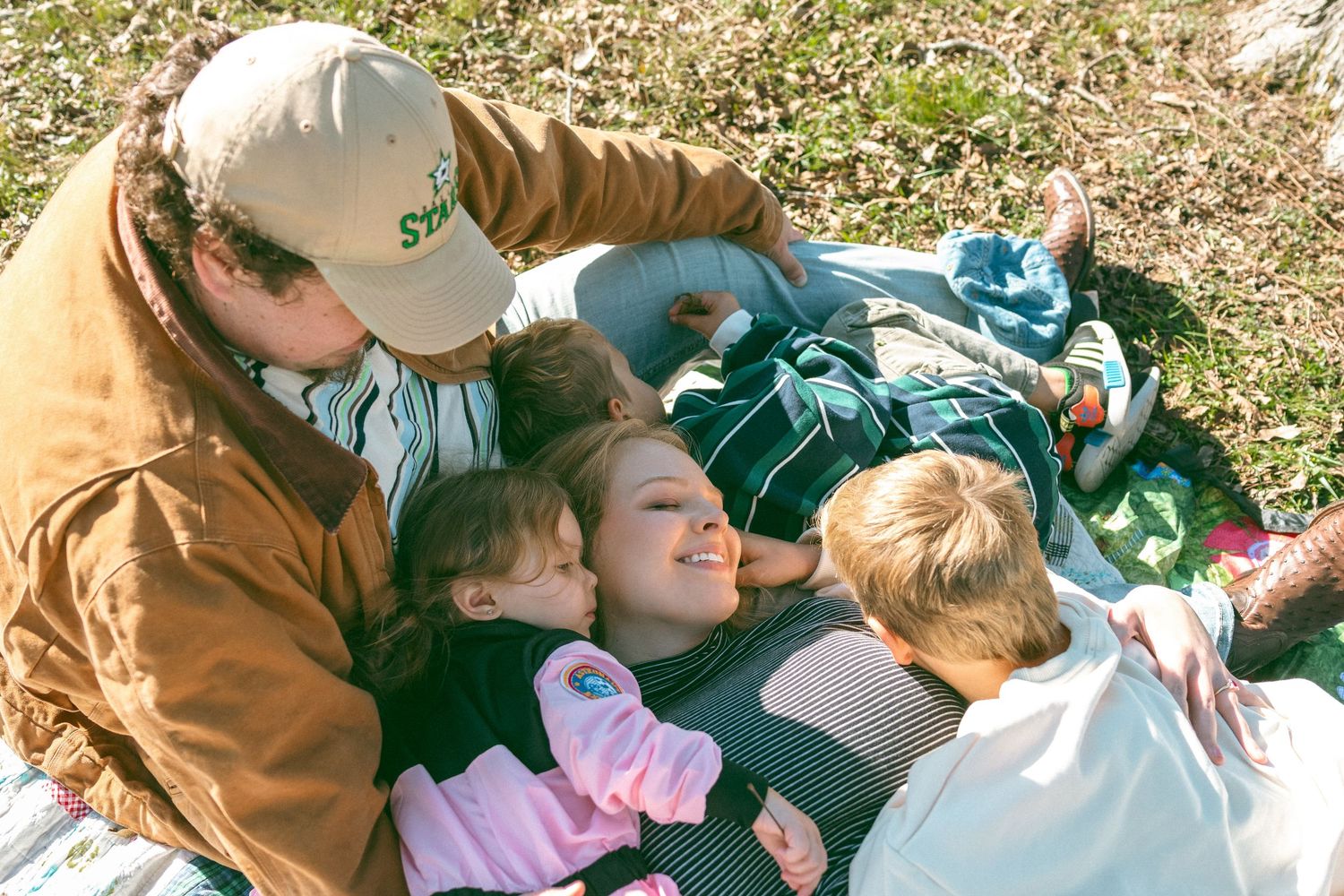 A family enjoys a tender moment together while relaxing outdoors on a sunny day.
