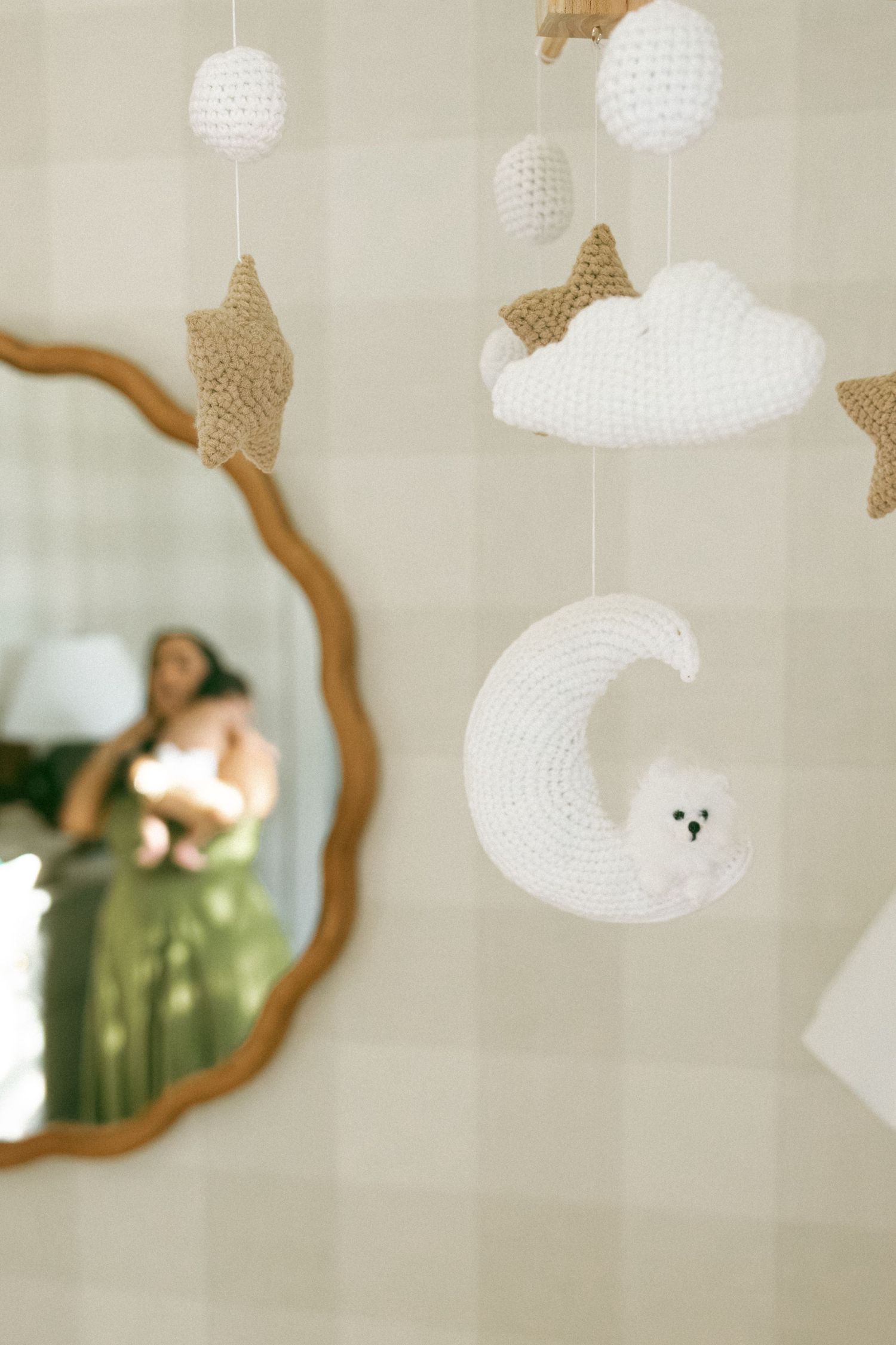 Delicate white and beige custom hanging decorations with trendy mirror reflection in soft focus. Dappled light nursery.