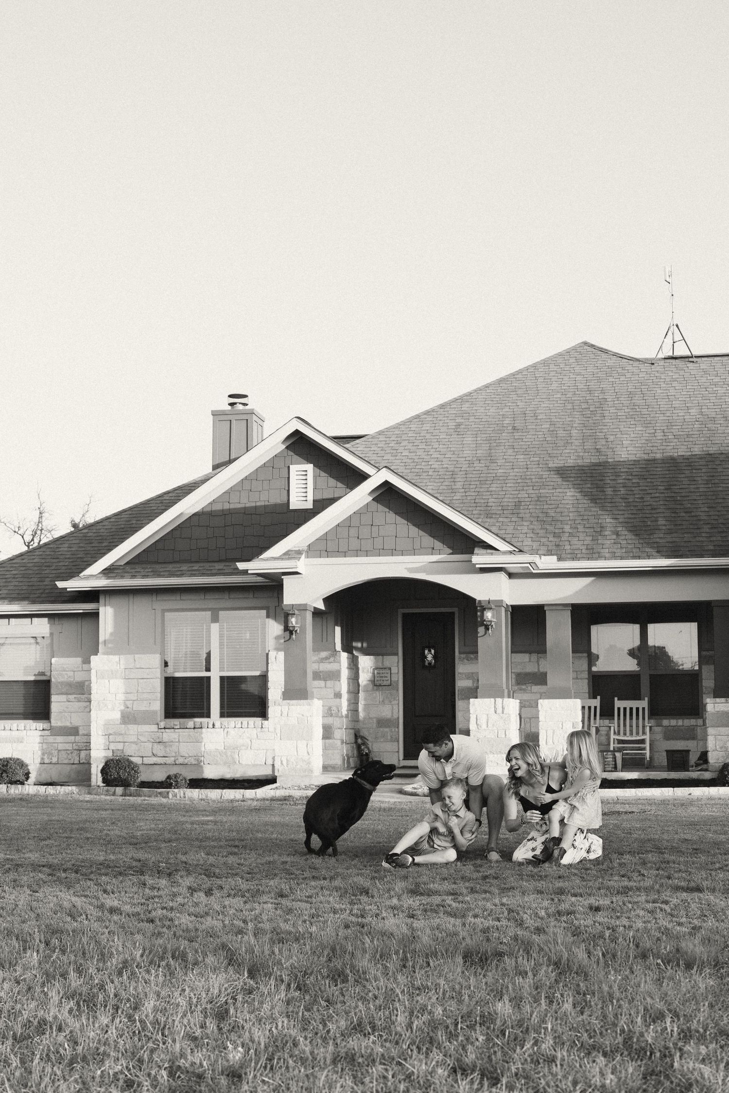 A classic craftsman style house with people and pets relaxing and playing on the front lawn.