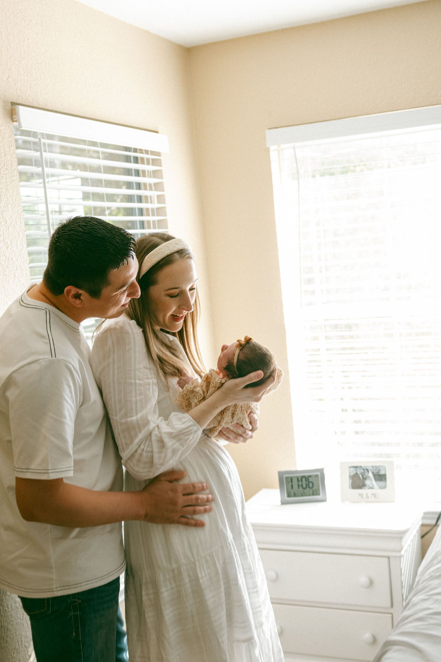 A couple in white clothing shares tender moments together in a bright sunlit room by the window.