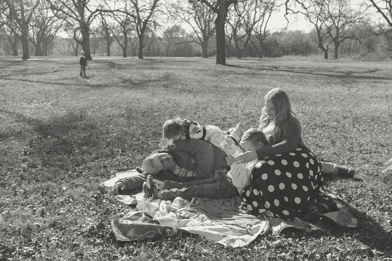 A vintage black and white photo shows people having a picnic under trees in a park setting.