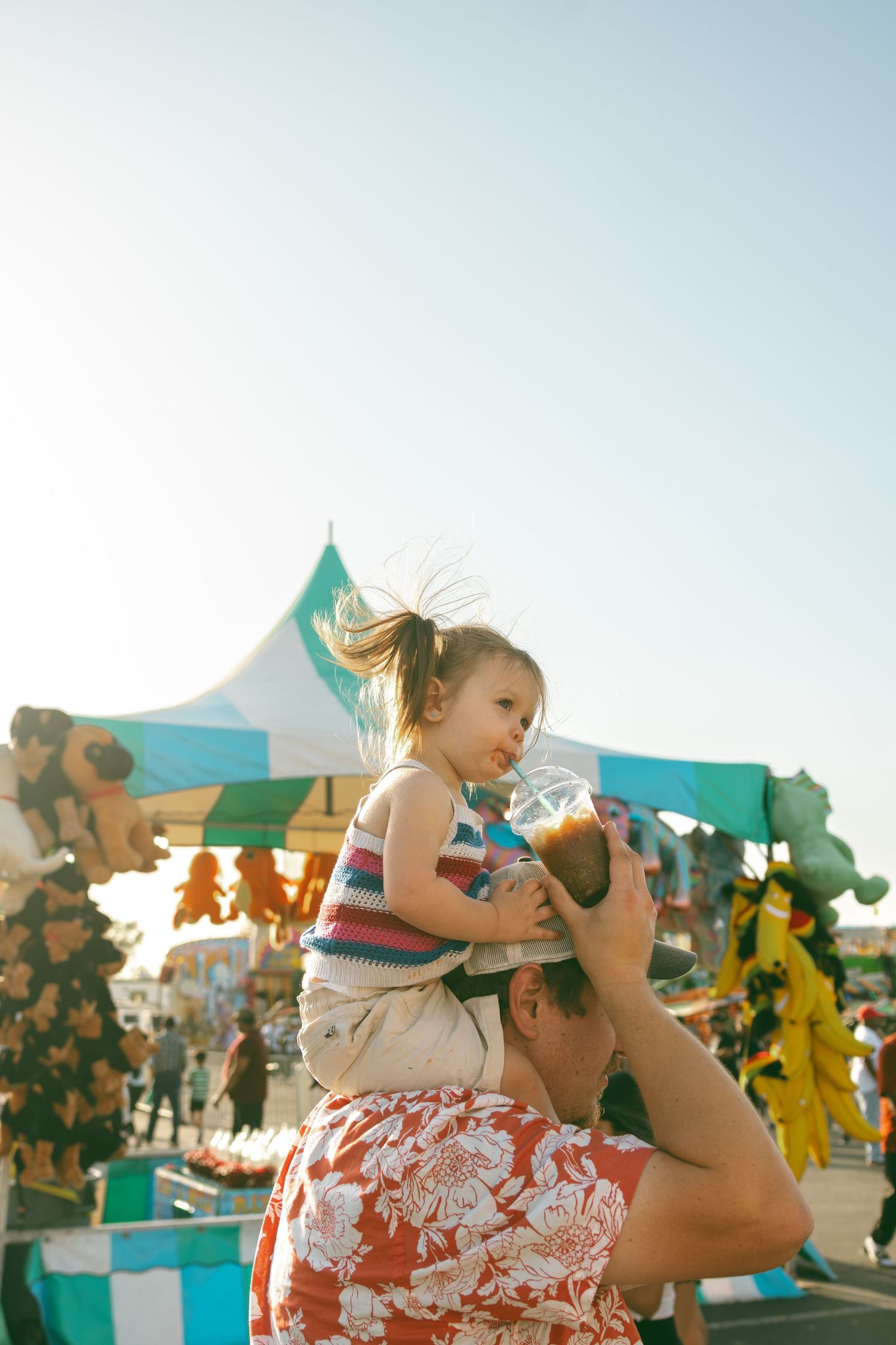Festive outdoor celebration at the Round Rock, TX carnival with bright prize booths, a cola slushie, and americana vibes against blue sky.