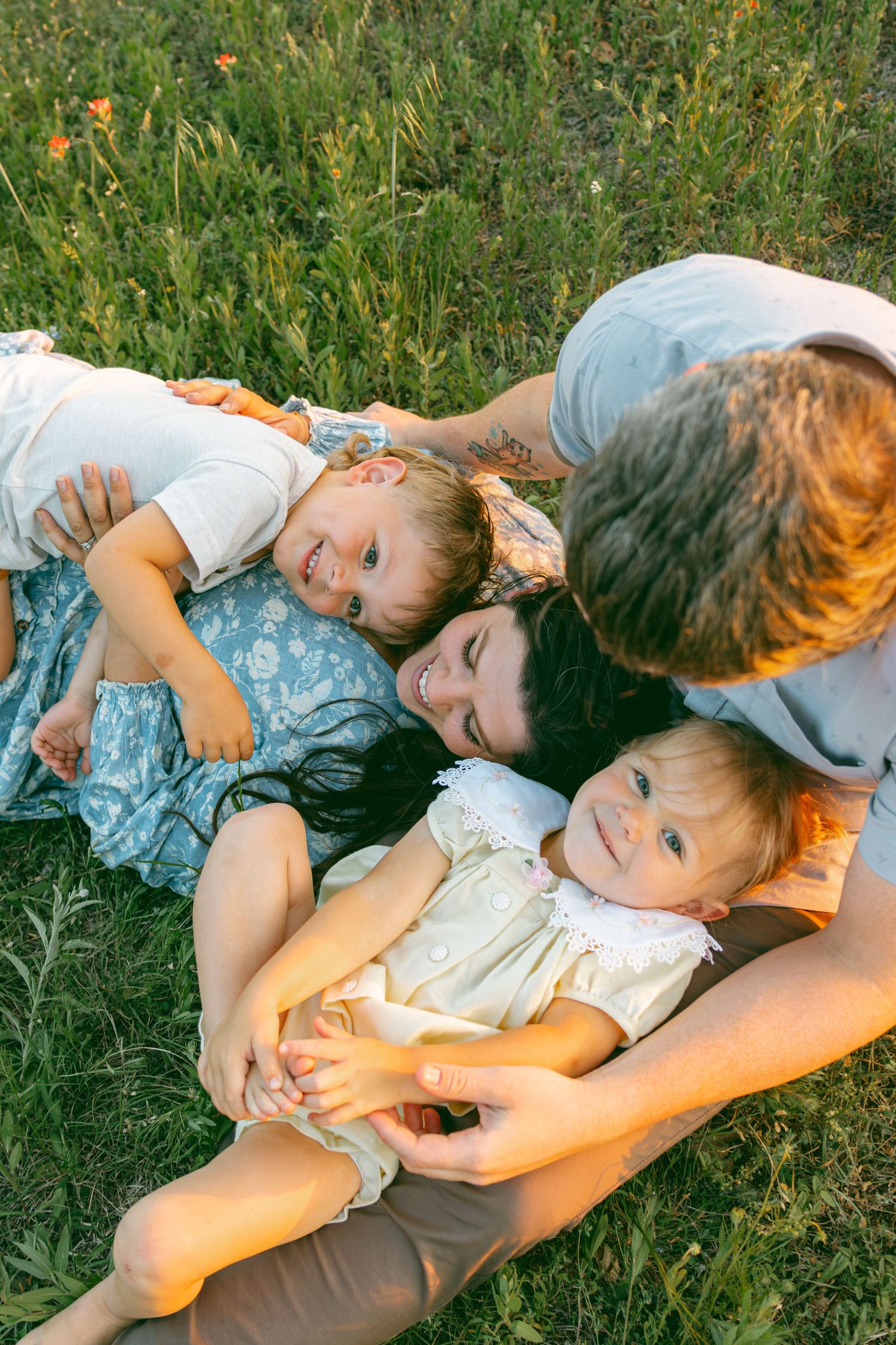A parent and child share a tender moment while laying in green grass on a sunny day.