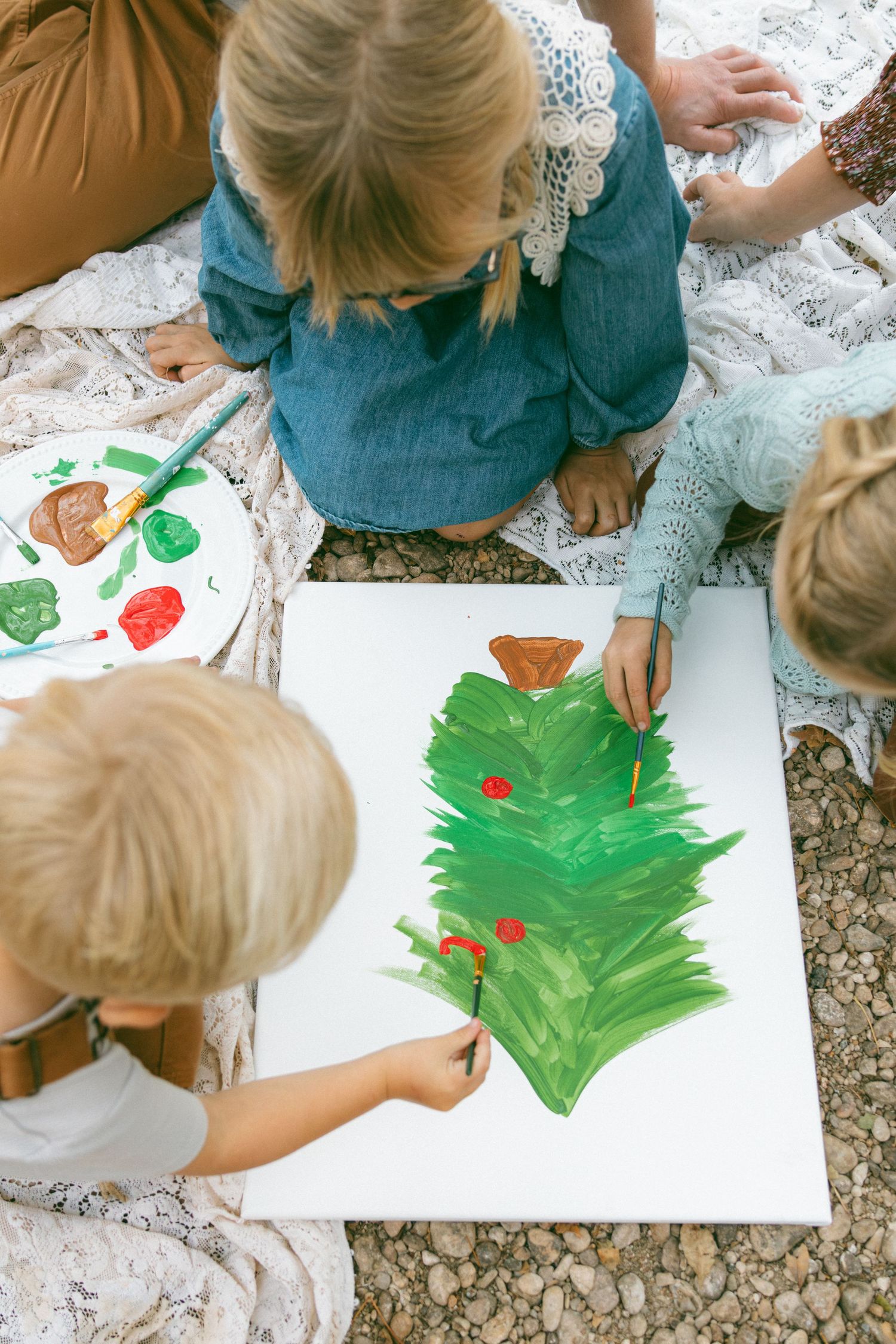 Children sit together painting a Christmas tree craft with red and green paint on white paper.