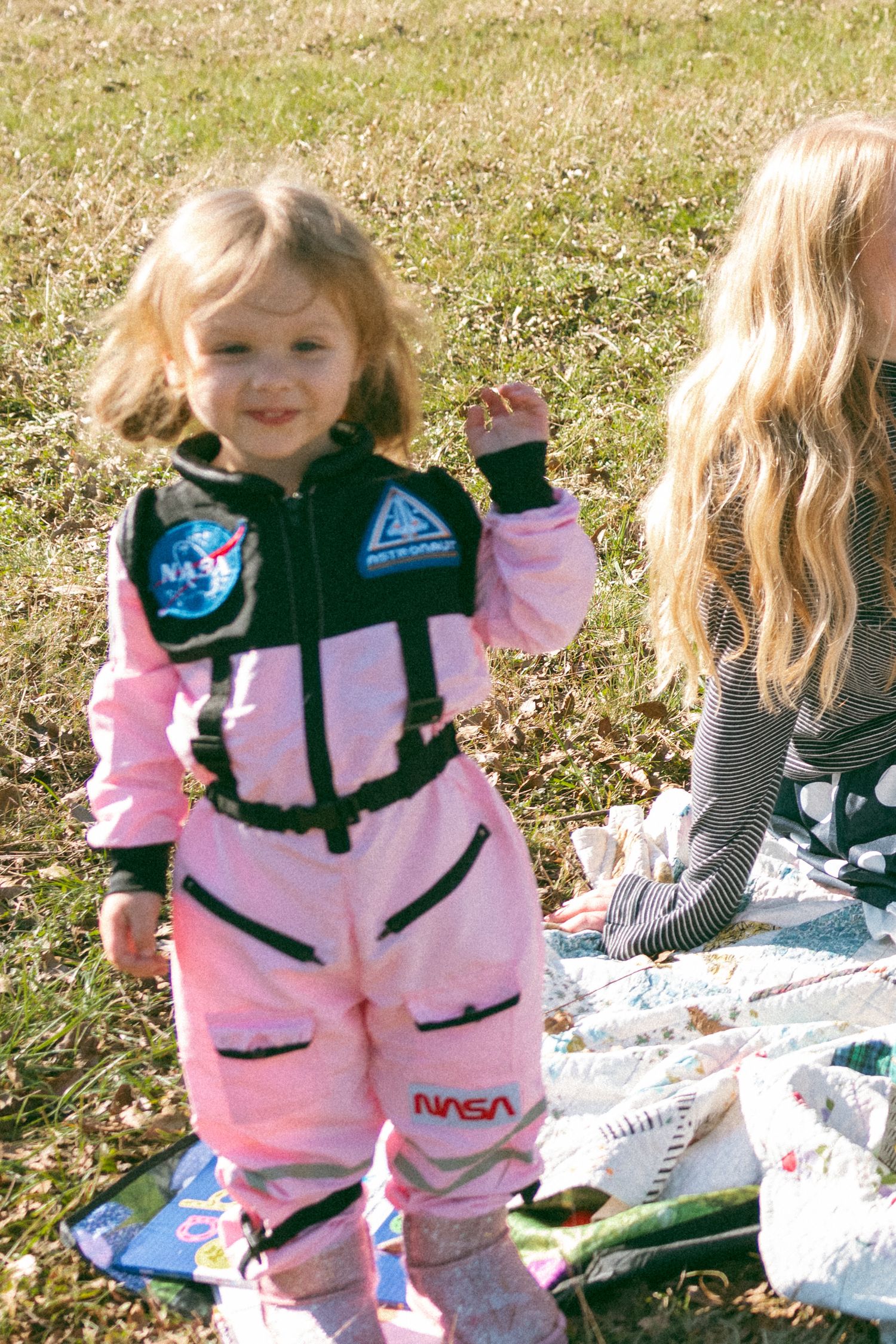 A series of photos showing a child wearing a pink and black NASA-themed outfit playing outdoors on a sunny day.