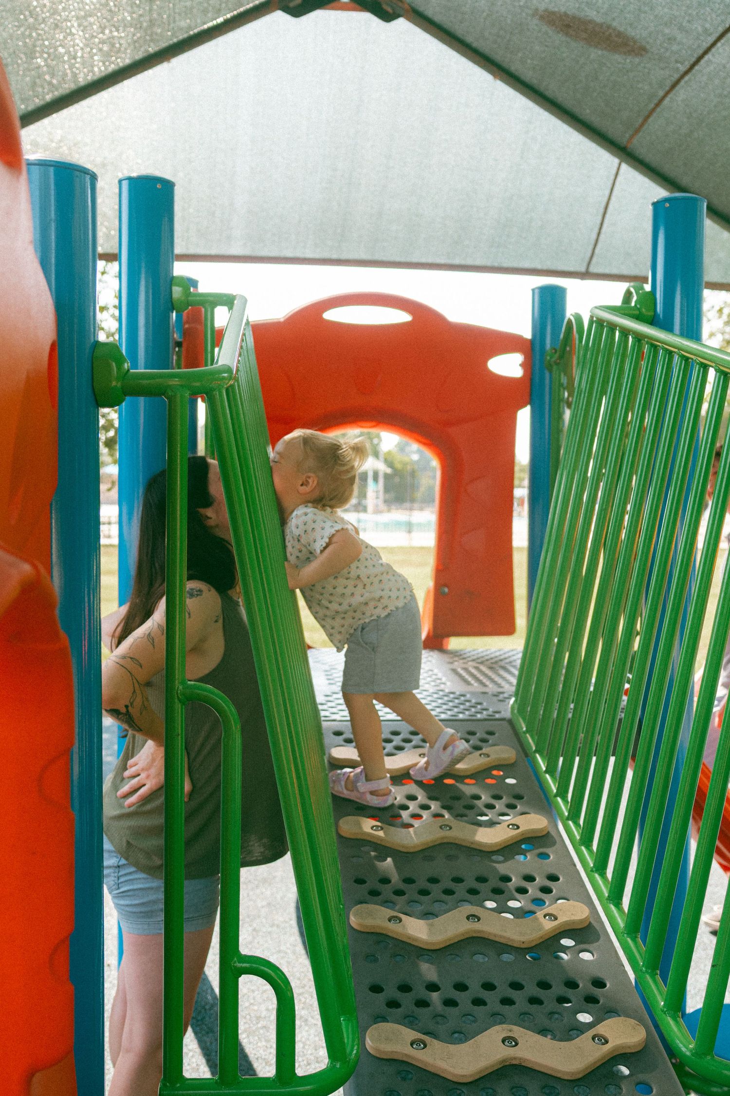 Mom and daughter kissing through the rails and playing on colorful playground equipment.