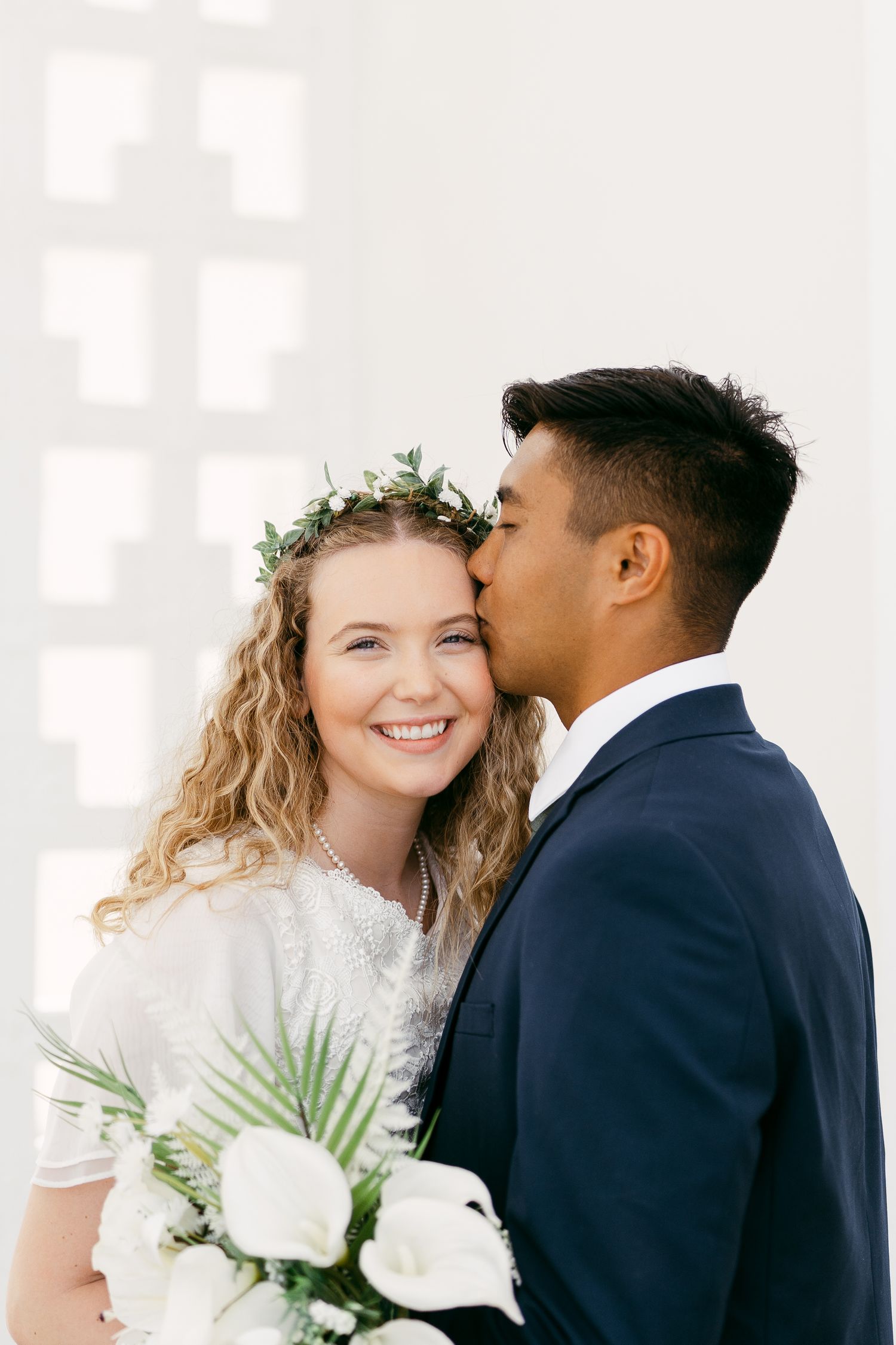 A joyful couple shares a tender moment during their wedding, with the bride wearing a floral crown and white dress.