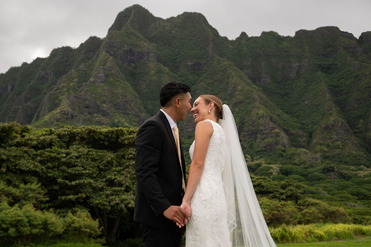 Bride and groom share a romantic moment with lush green Hawaiian mountains in the background on their wedding day.
