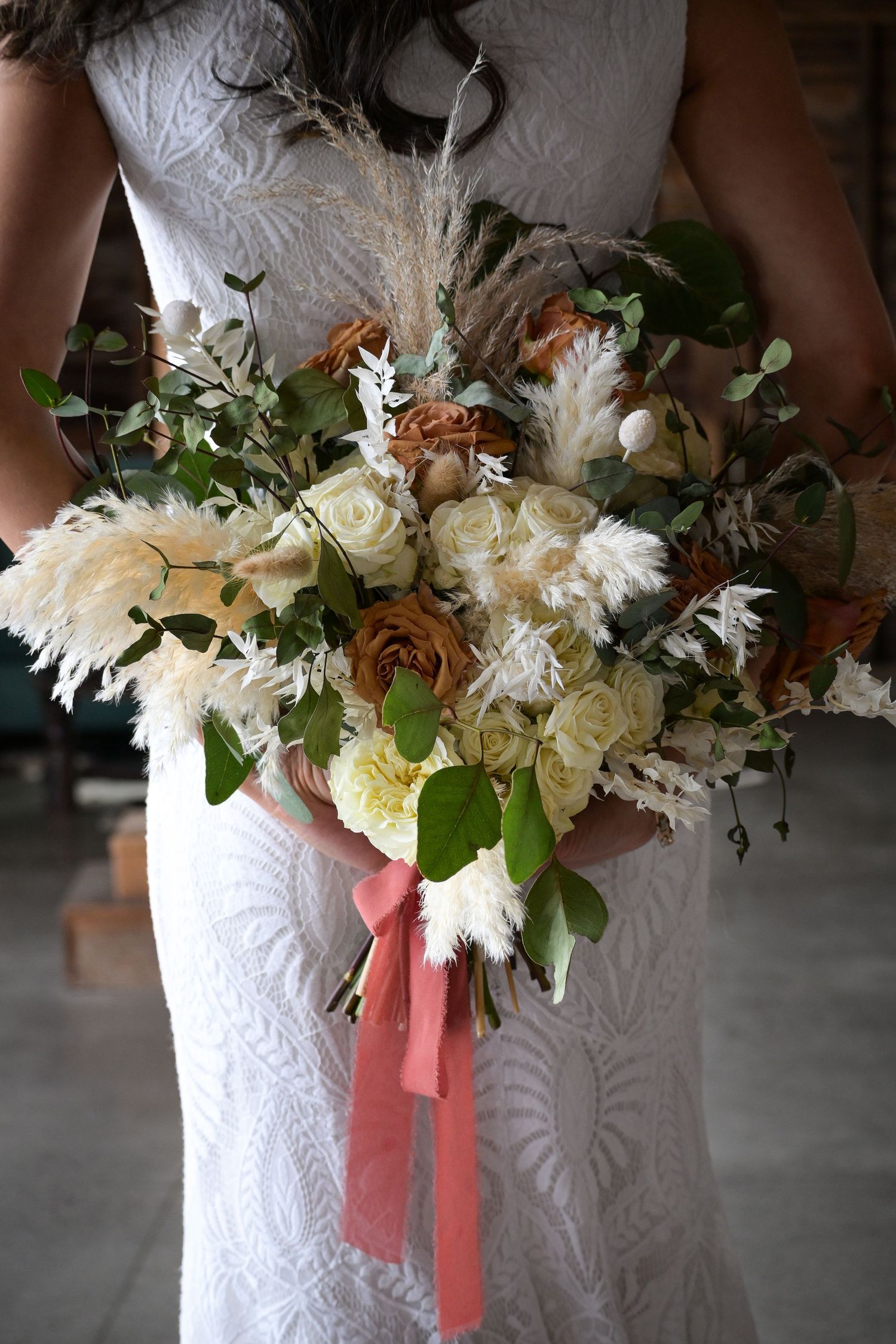 A romantic bridal bouquet with white roses, dried pampas grass and coral ribbons.