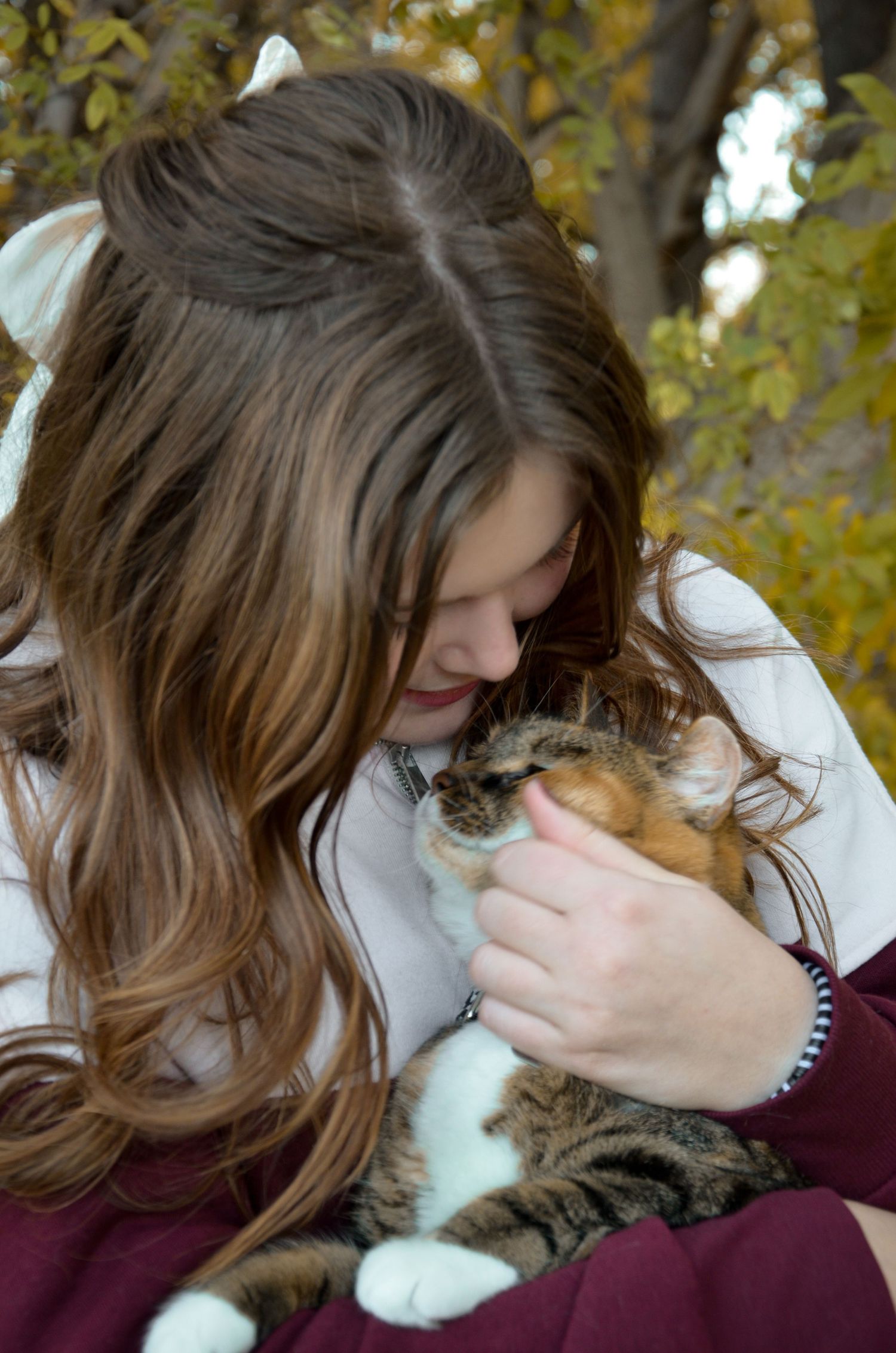 Person in white sweater cuddles with calico cat outdoors.