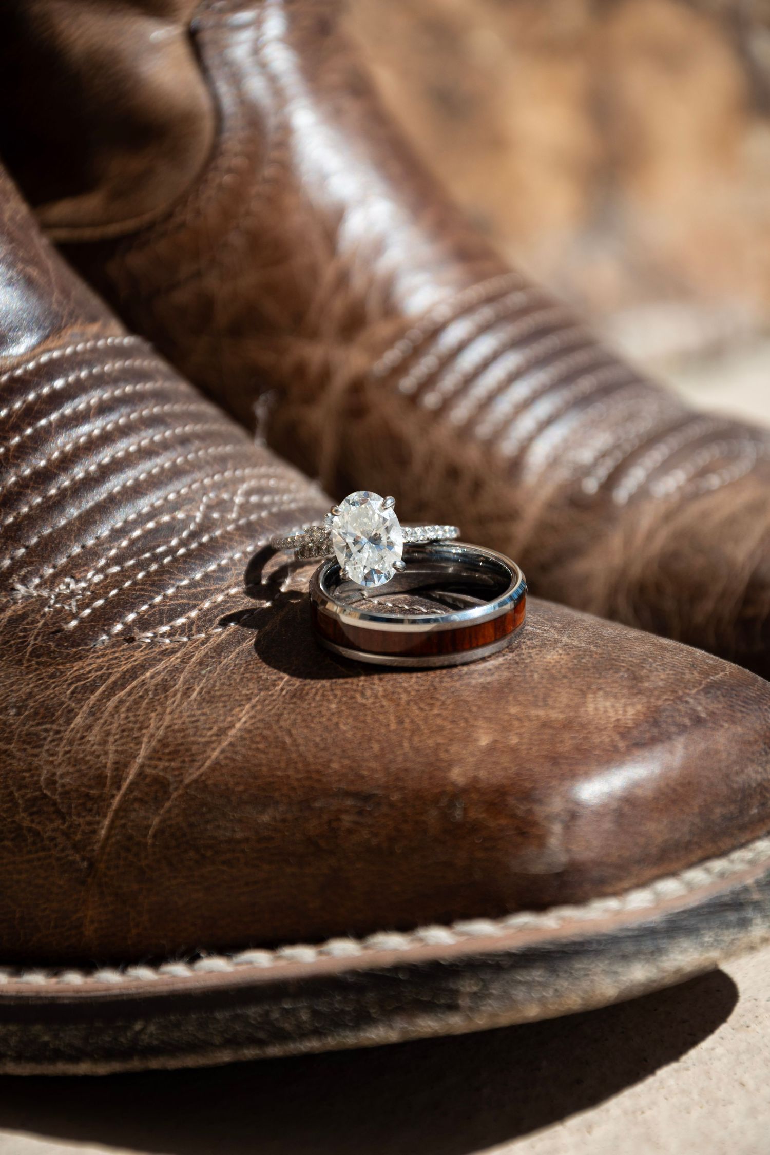 A diamond engagement ring rests delicately on a brown leather cowboy boot with intricate stitching details.