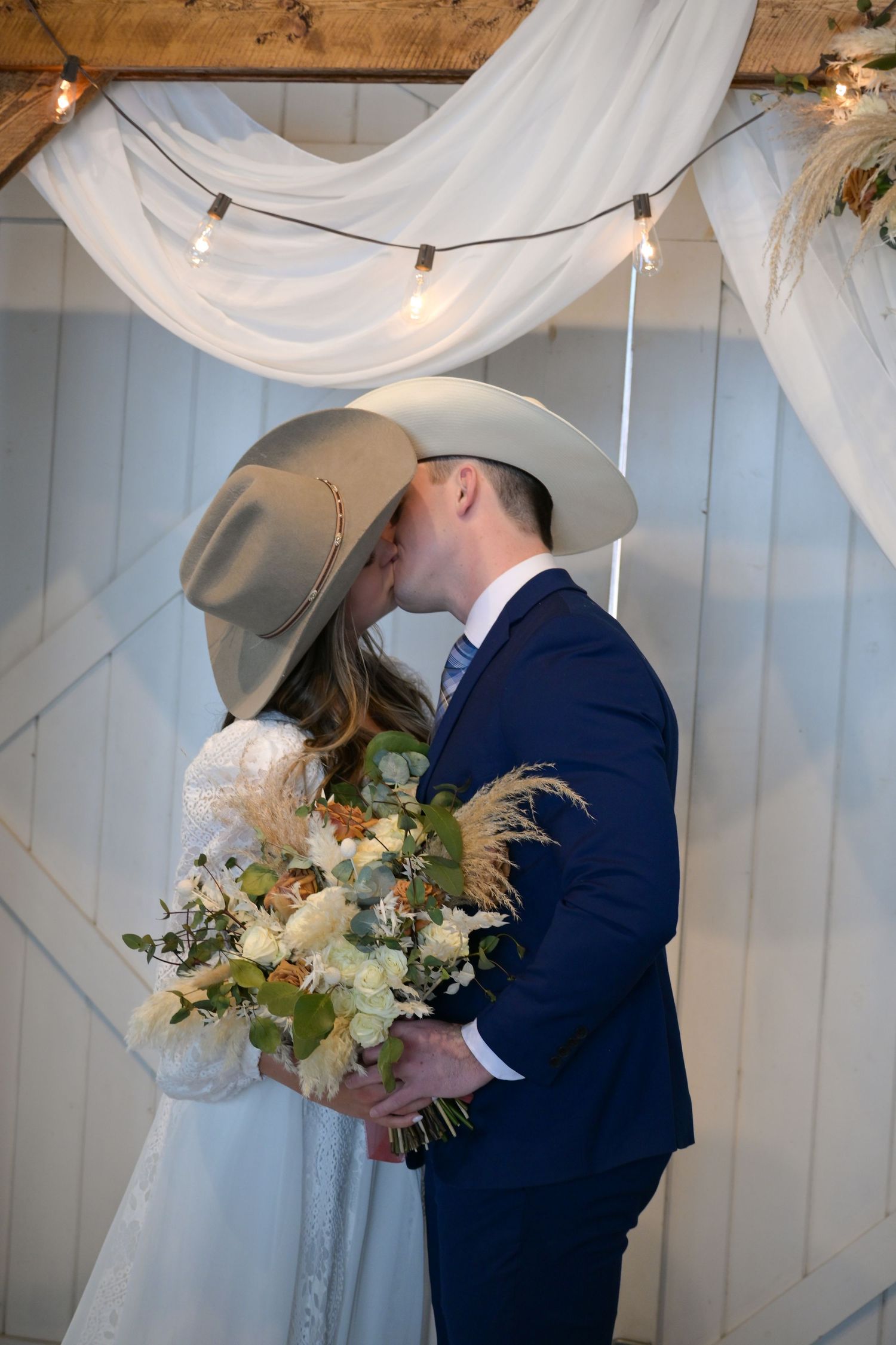A couple sharing a romantic kiss under white fabric draping and string lights.