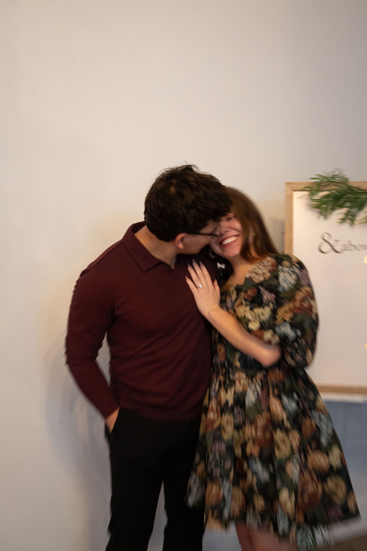 A romantic couple sharing a tender moment and laughing together indoors against a light wall.