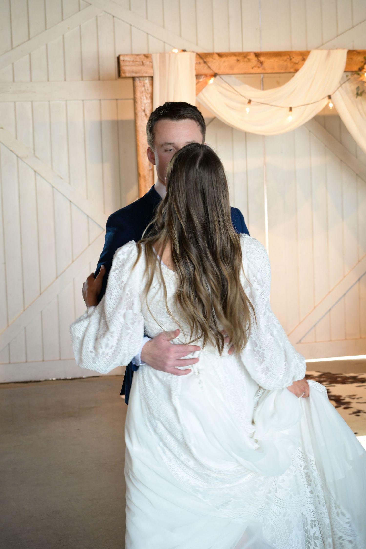 Couple shares intimate moment in rustic white barn venue during wedding photoshoot.
