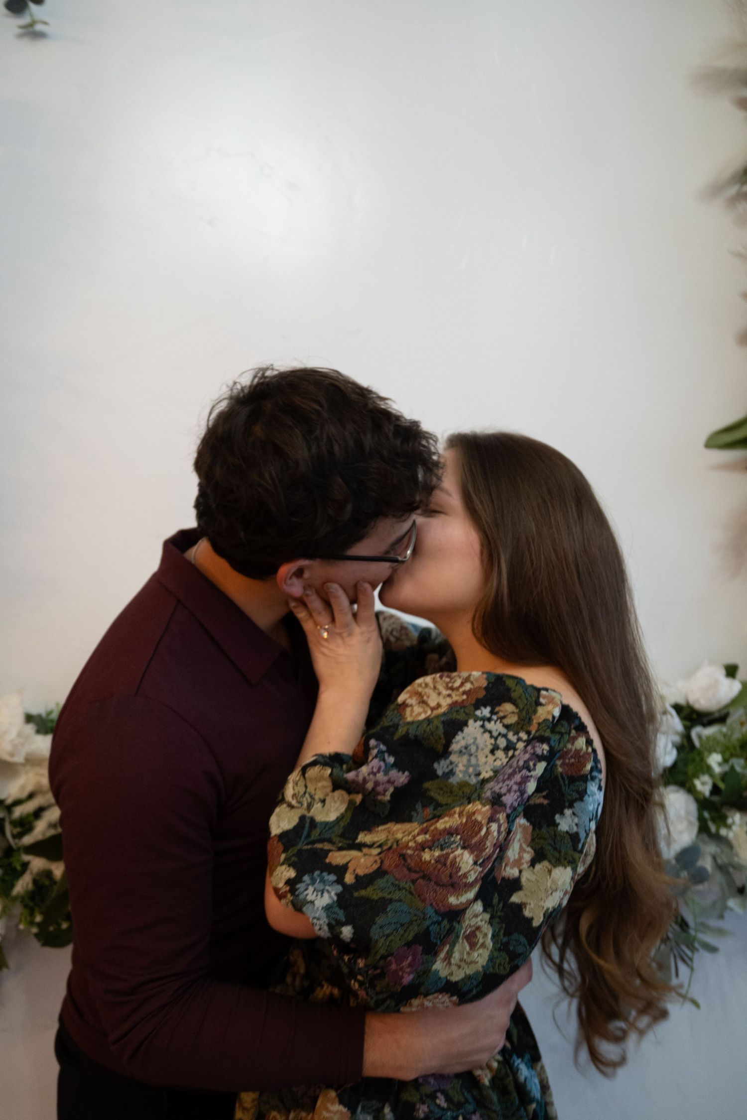 Intimate romantic moment against white wall with subtle floral decorations.