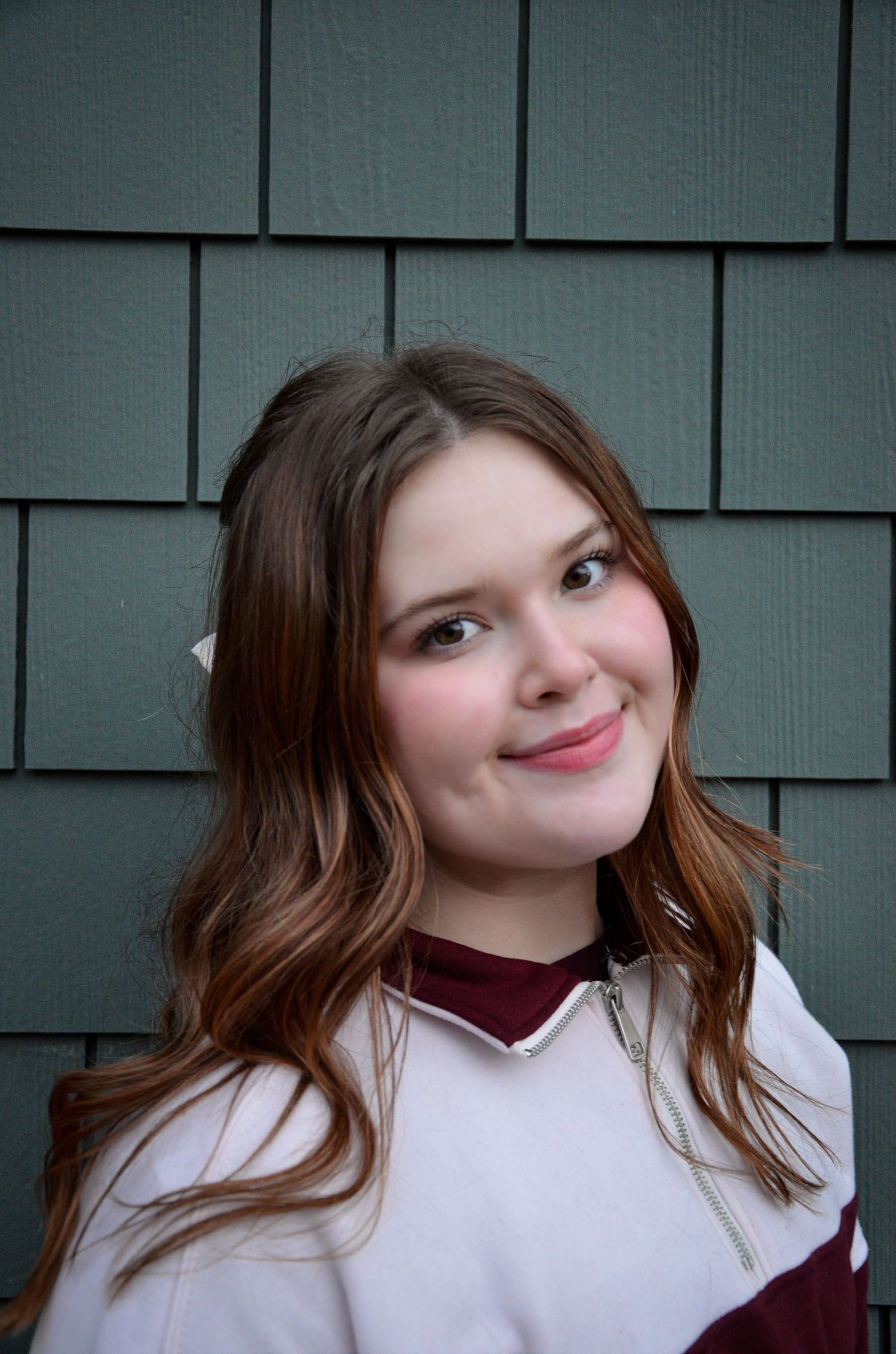 Person in white and maroon top poses against gray shingled wall.