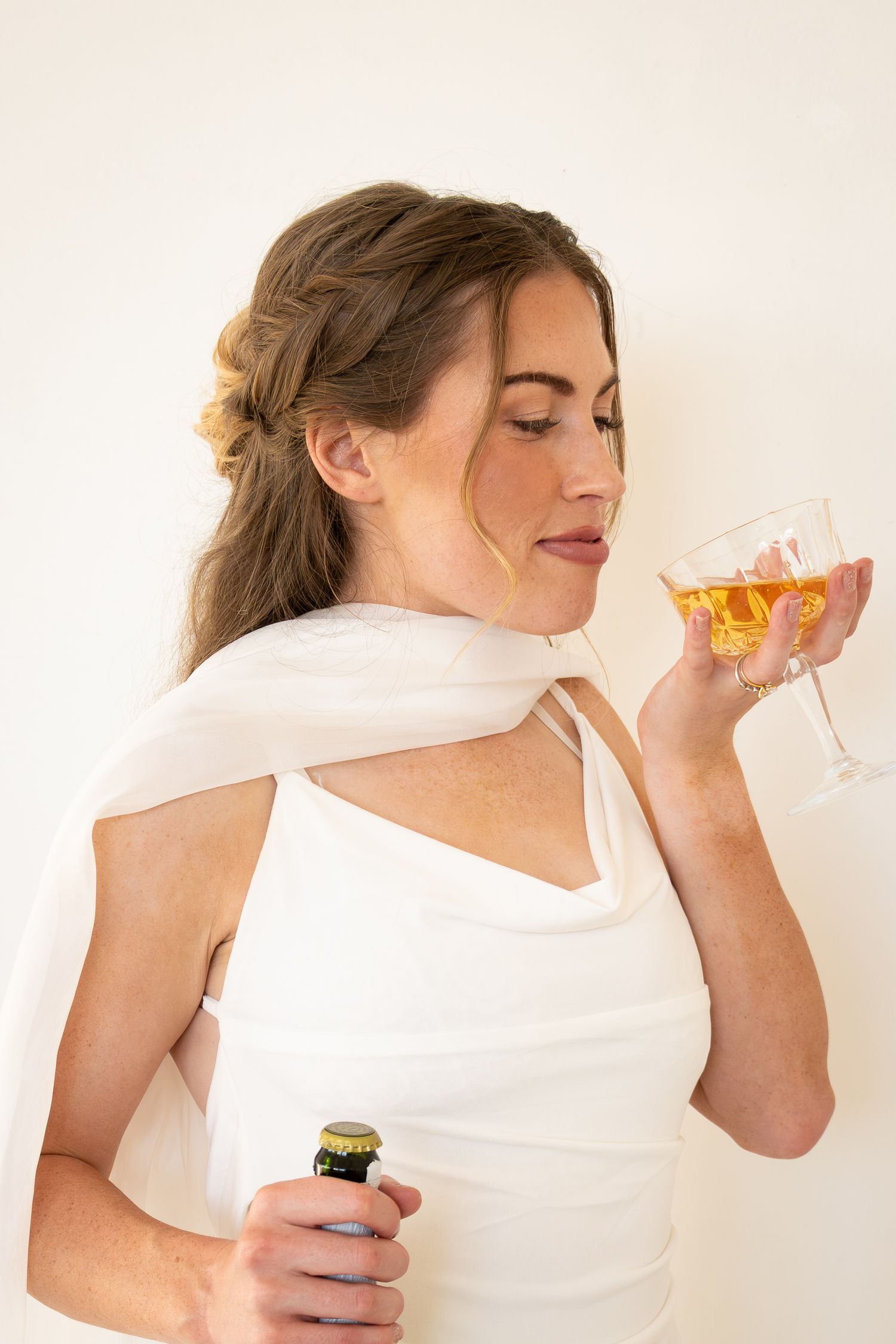 Elegant woman in white dress holding a wine glass and beer bottle, enjoying a drink at a formal event.
