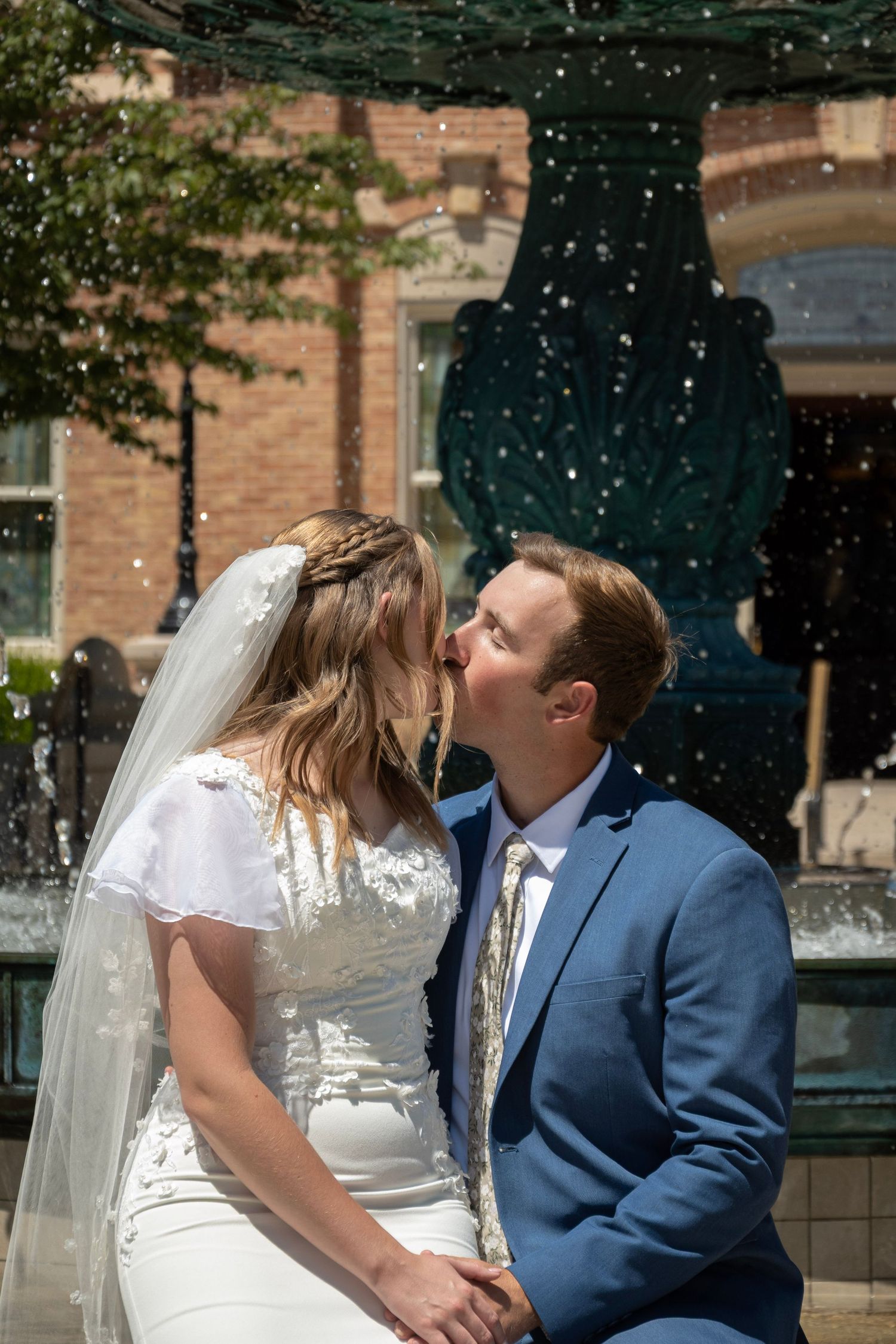 A bride and groom share a kiss during their wedding ceremony as water droplets sparkle in the sunlight.