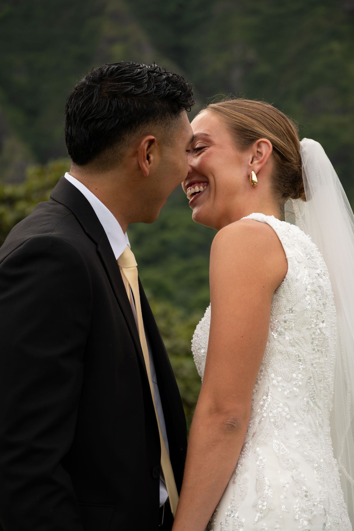 A joyful bride and groom share a romantic moment, laughing together on their wedding day outdoors.